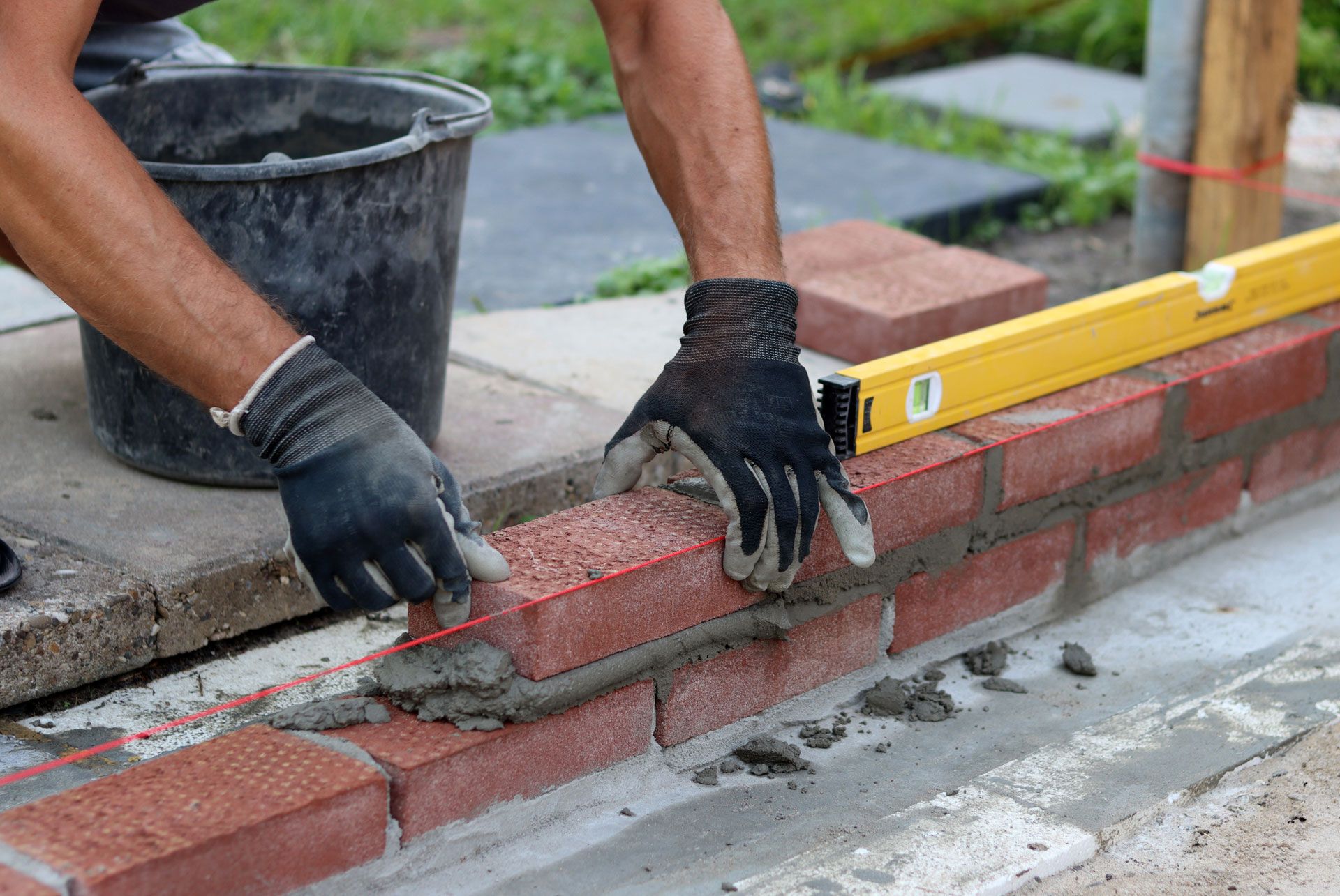 Worker laying red bricks with mortar beside a yellow level on a construction site