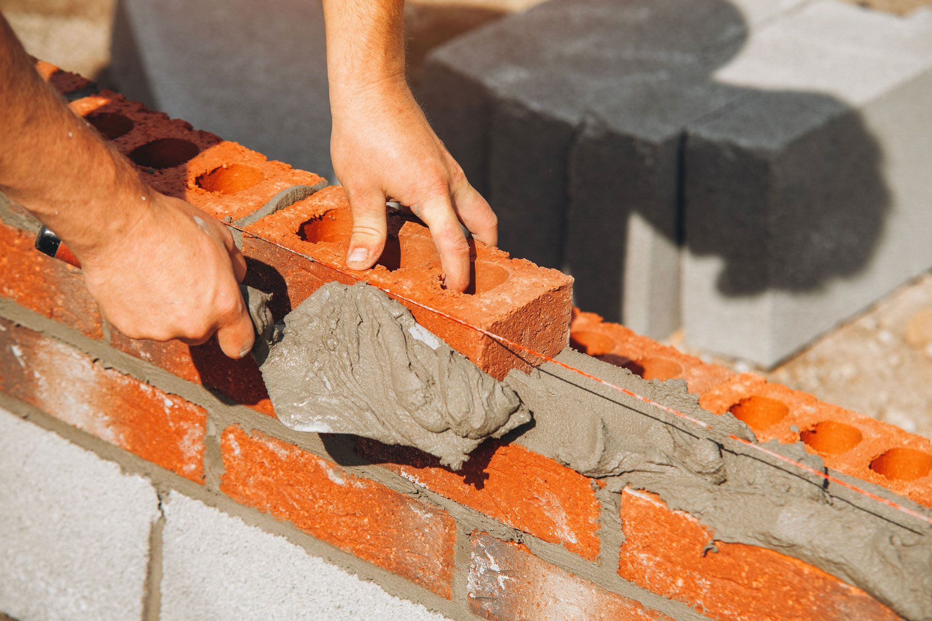 Hands spreading mortar between orange bricks during wall construction