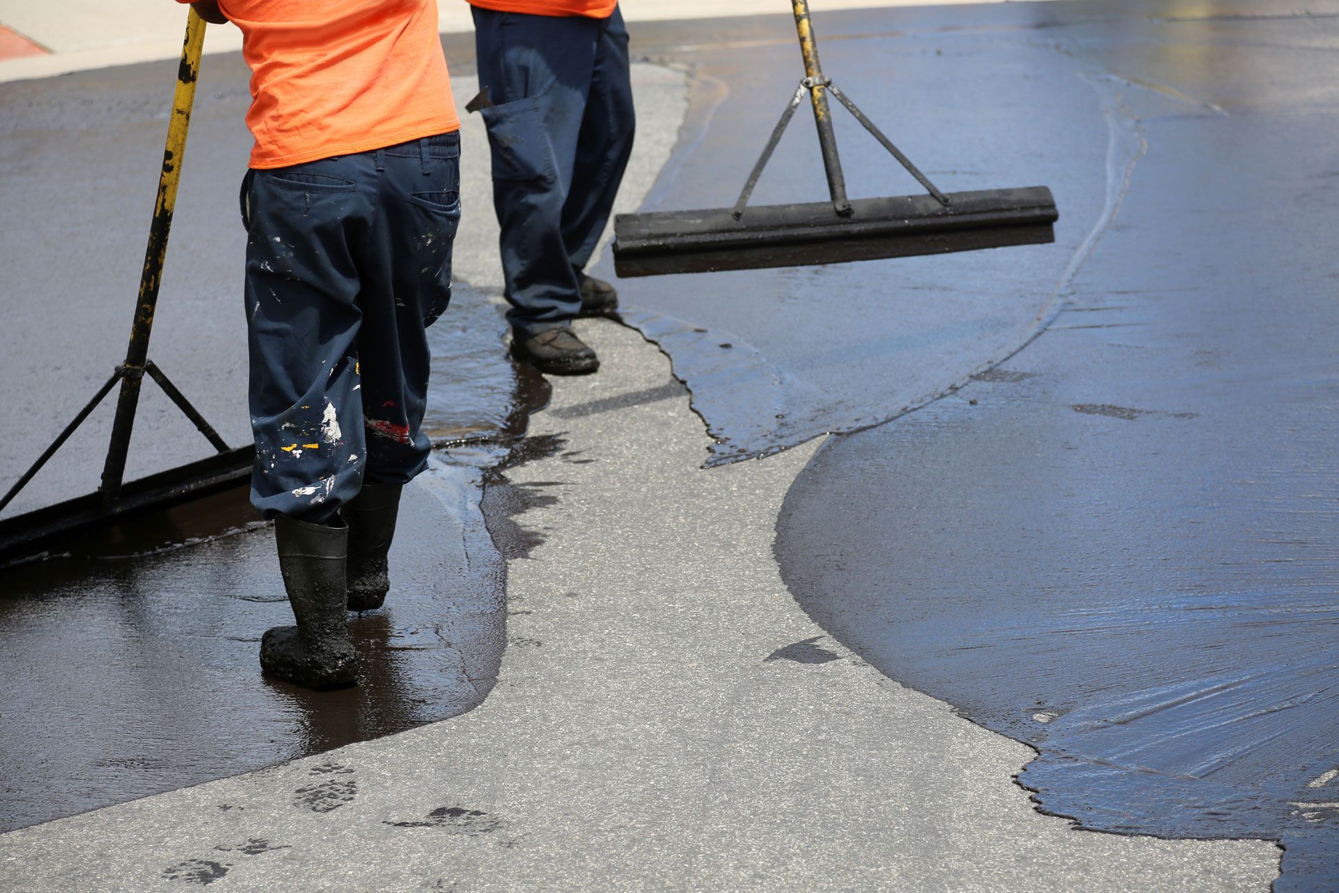 Workers smoothing wet concrete with squeegees on a driveway or road surface