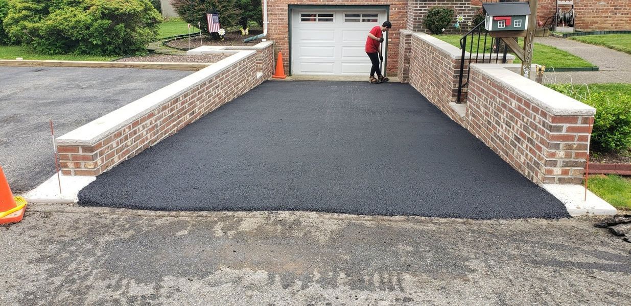 Freshly paved asphalt driveway with brick walls and a person working on the surface.