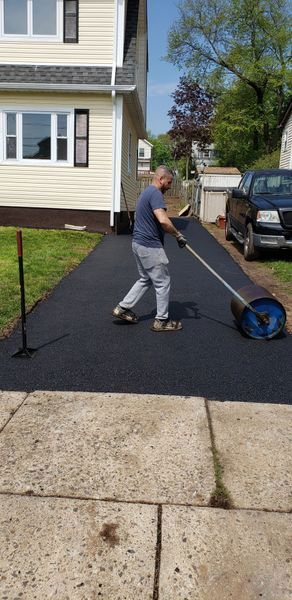 A man rolling fresh asphalt on a driveway next to a two-story beige house.