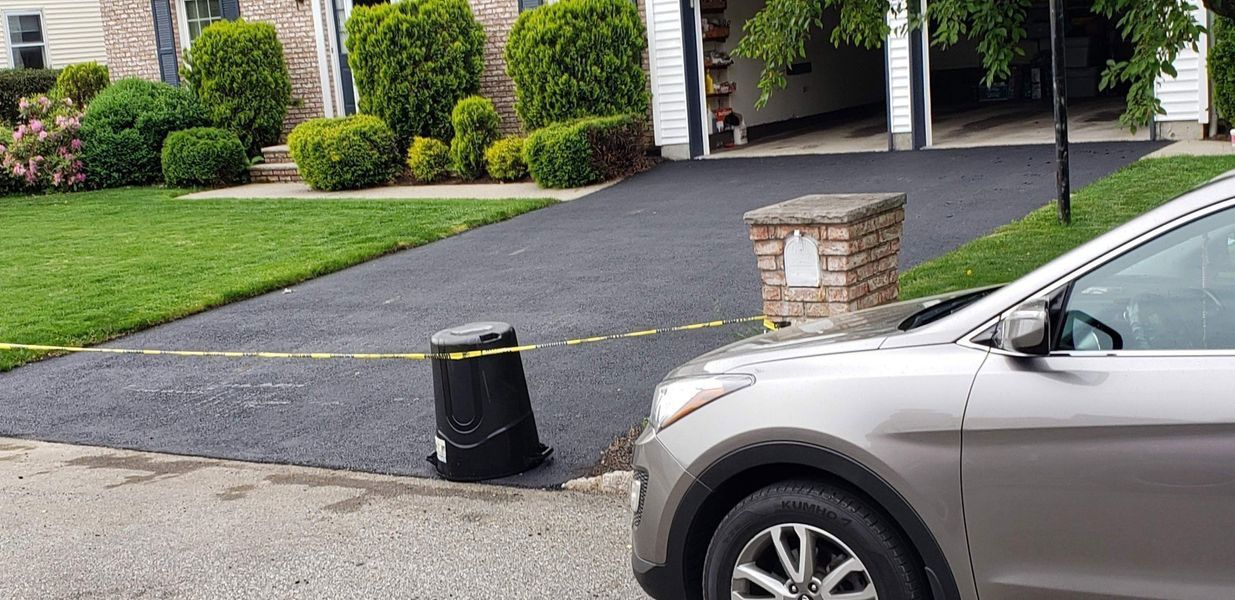 A silver car parked in front of a house with a black driveway. Yellow caution tape is strung across the driveway.