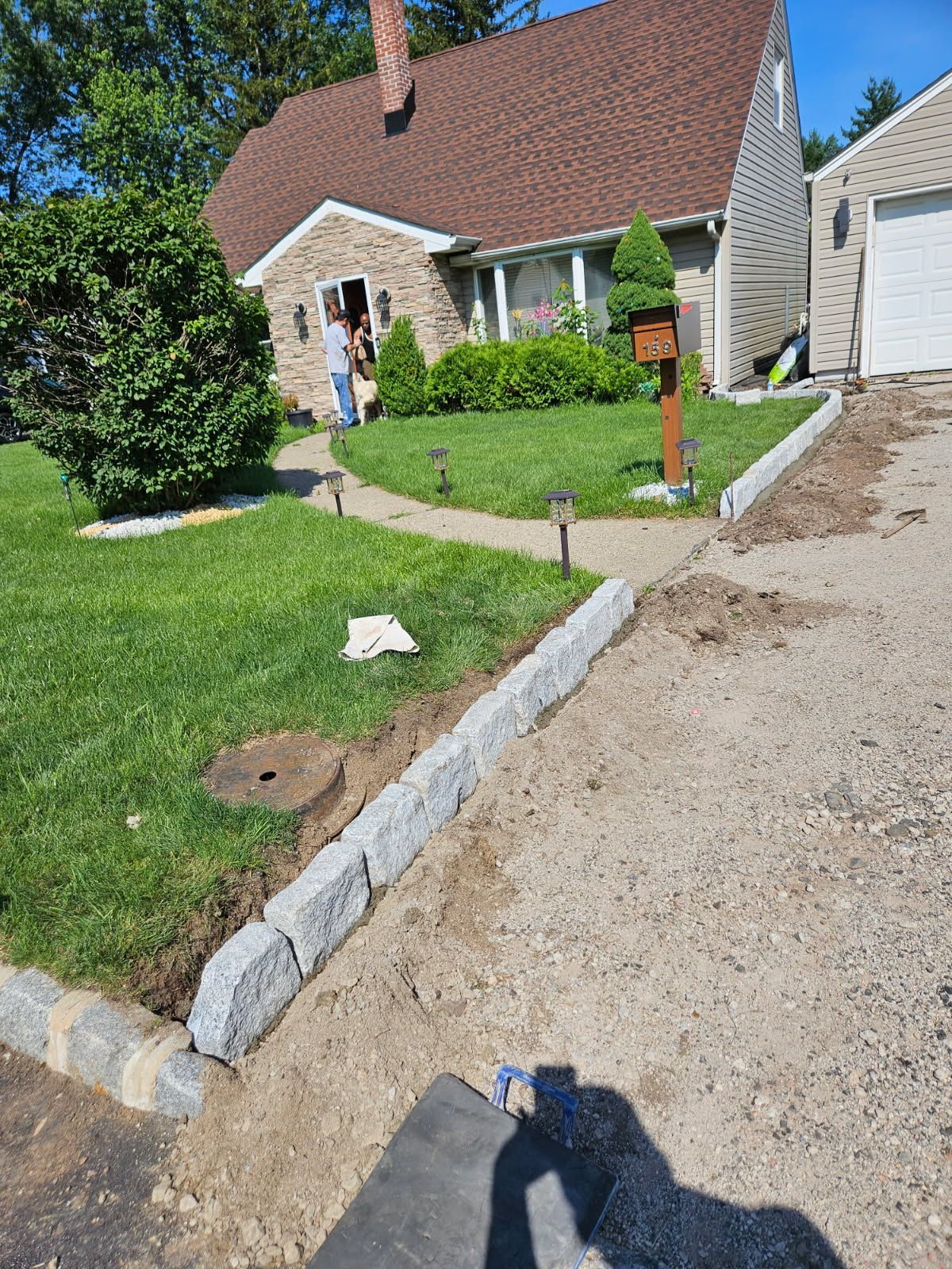 House with sloped lawn and gravel driveway, a person near the front door, and a dog in the grass.