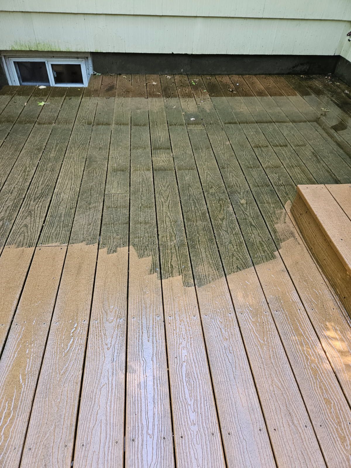 Weathered wooden deck with a large dark wet stain near the house wall and basement vent.