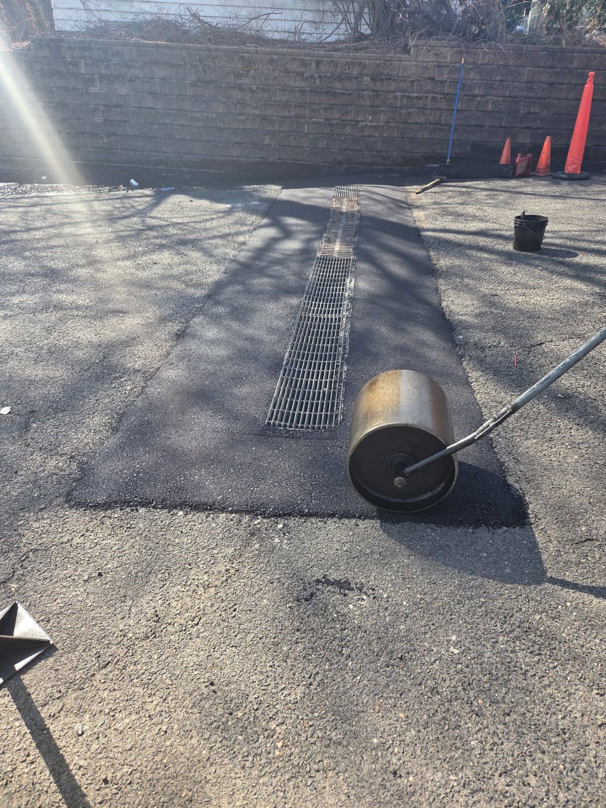 Roofing work with rolled roofing material on a sunlit asphalt surface, cones and tools nearby