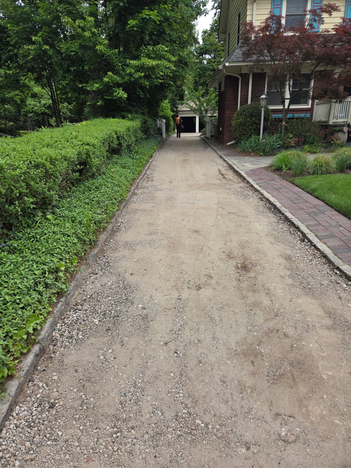 Gravel path between green hedges and trees, beside a house with a porch.