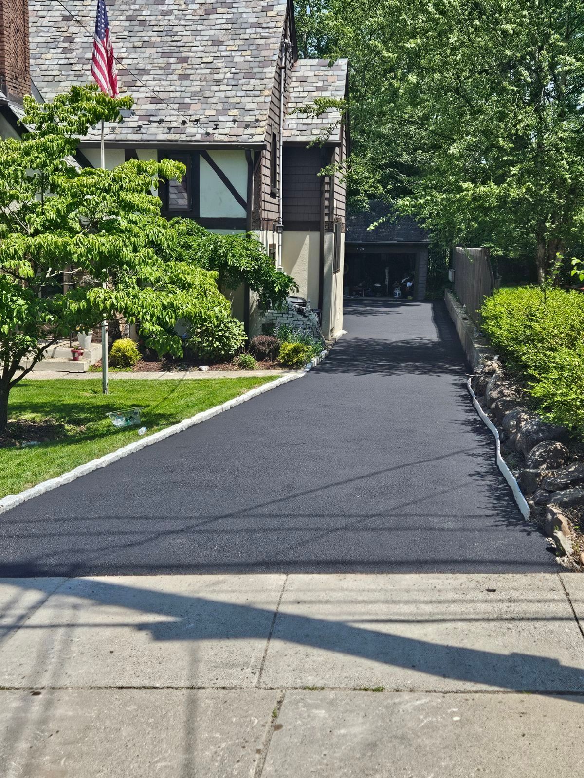 Freshly paved driveway leading to a house, with an American flag and green shrubs along the side.