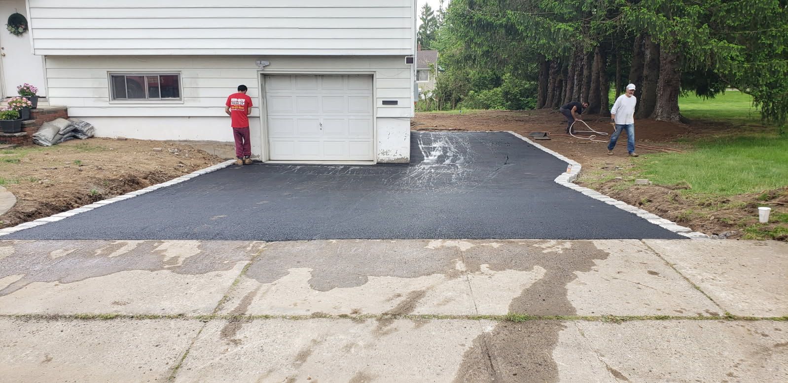 Driveway with a new dark asphalt section connecting to the older, lighter asphalt road, in front of a two-car garage.