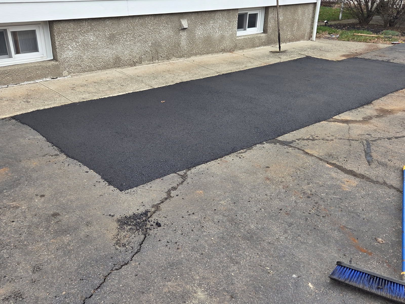 Freshly paved black asphalt patch beside a building on a cracked driveway