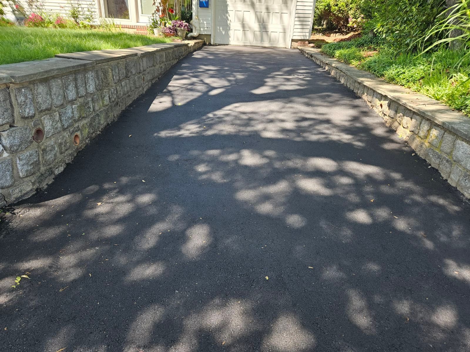 Shaded asphalt driveway bordered by low stone walls leading to a house garage