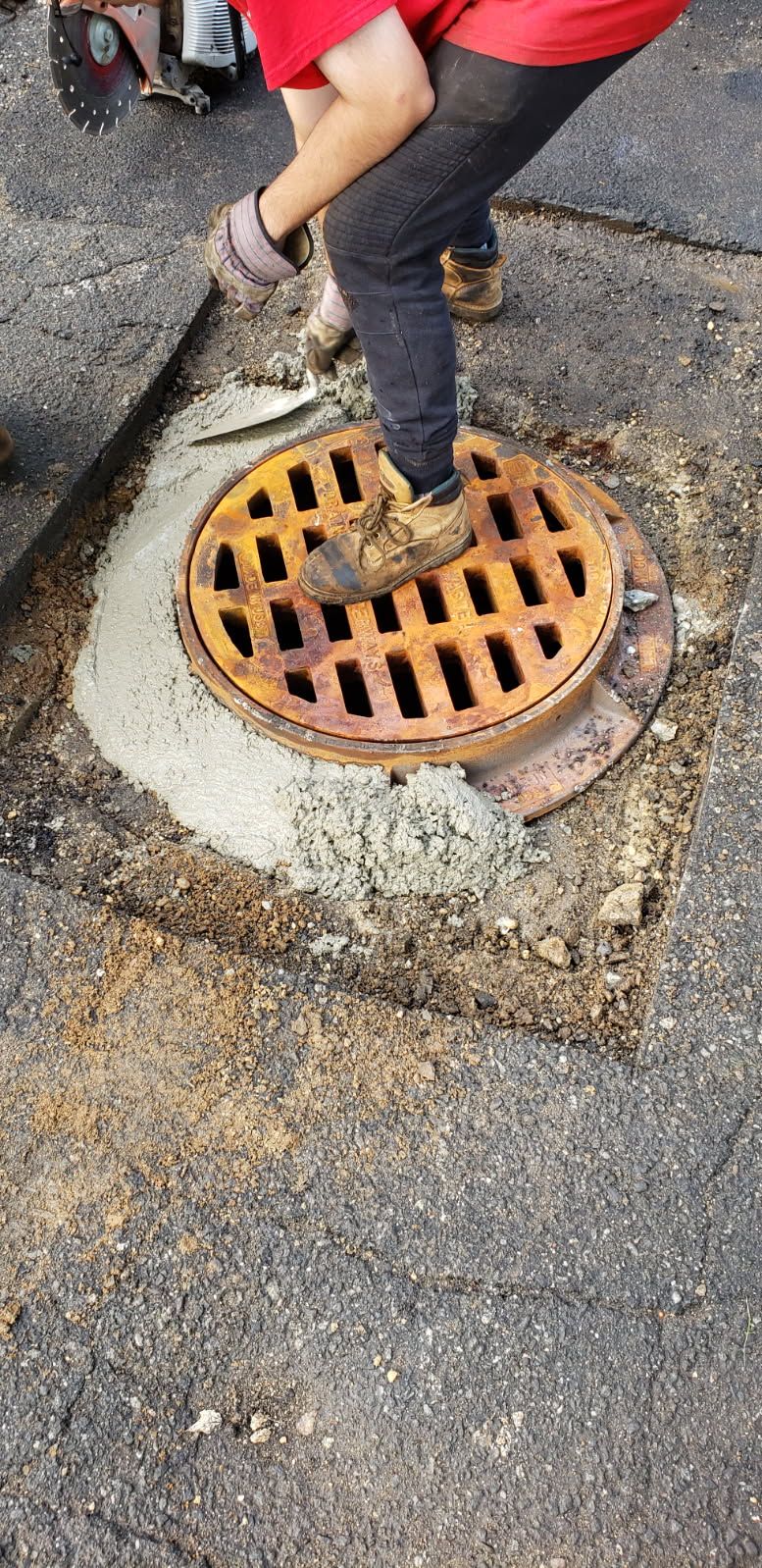 Worker stepping on a rusty storm drain grate in a paved street