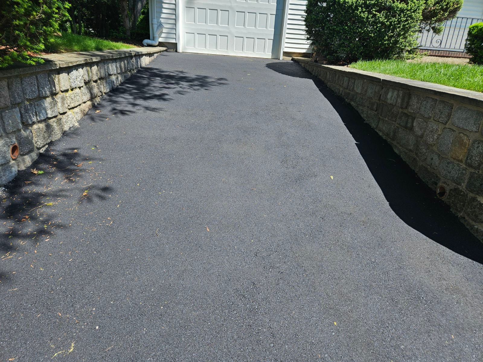 Black asphalt driveway between stone retaining walls leading to a white garage door.