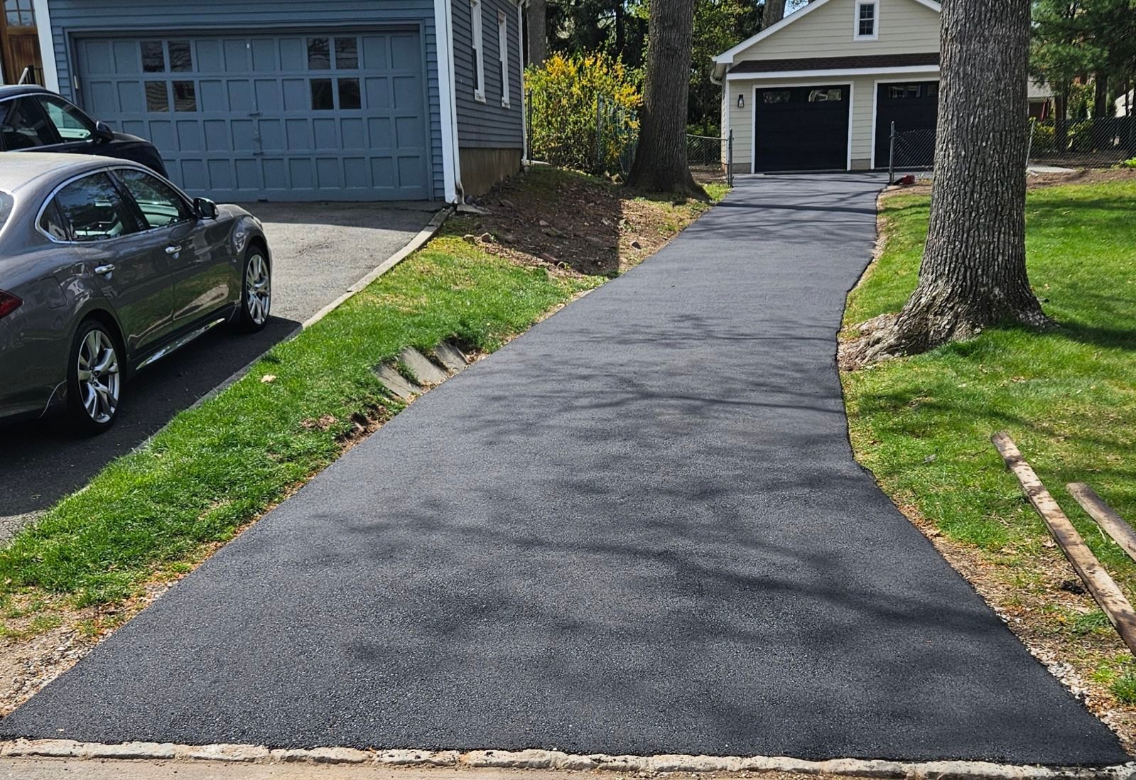 Freshly paved black driveway leading to a garage beside a parked car and green lawn