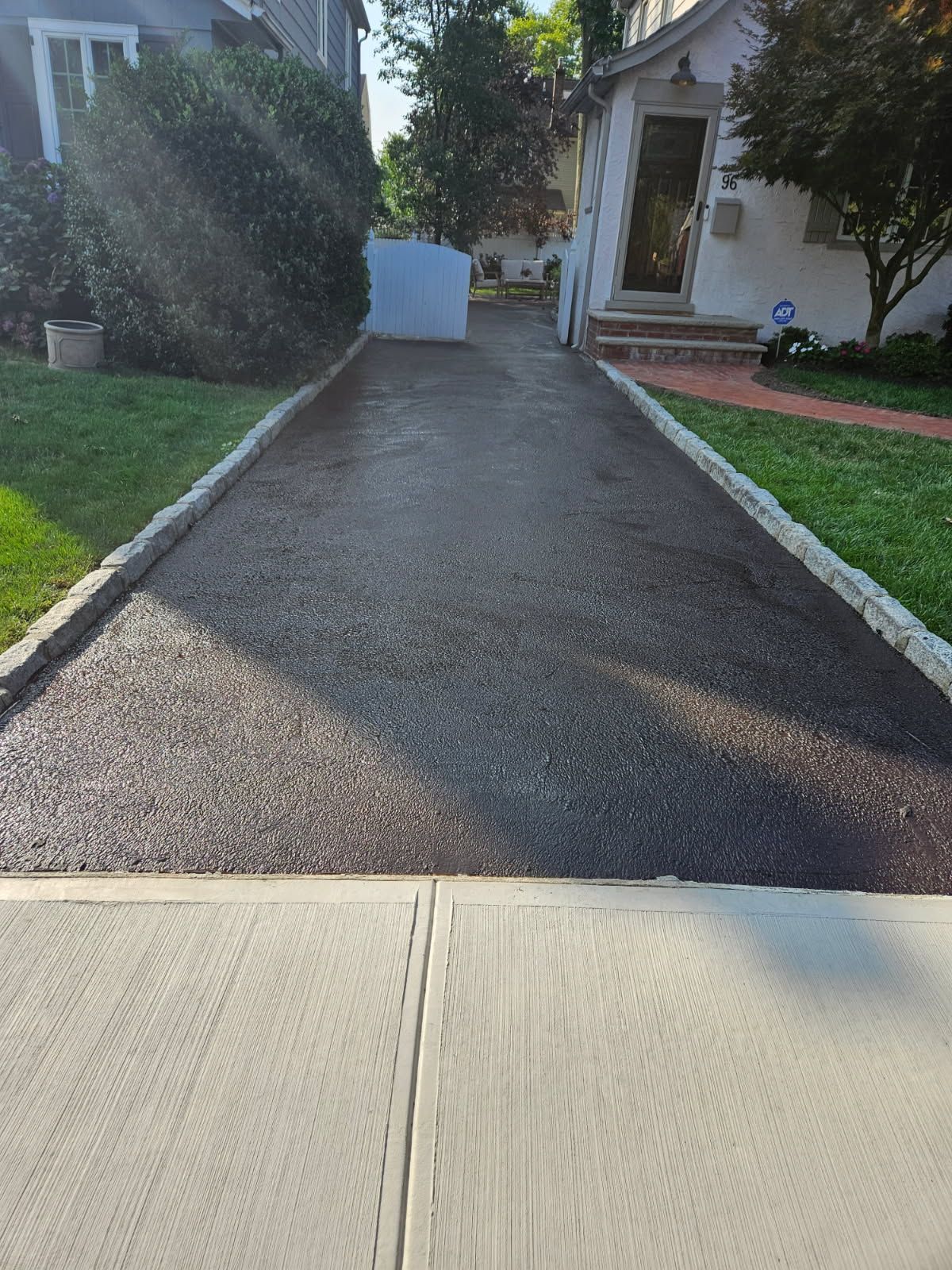 Driveway leading to a house entrance, with grass and bushes on both sides.