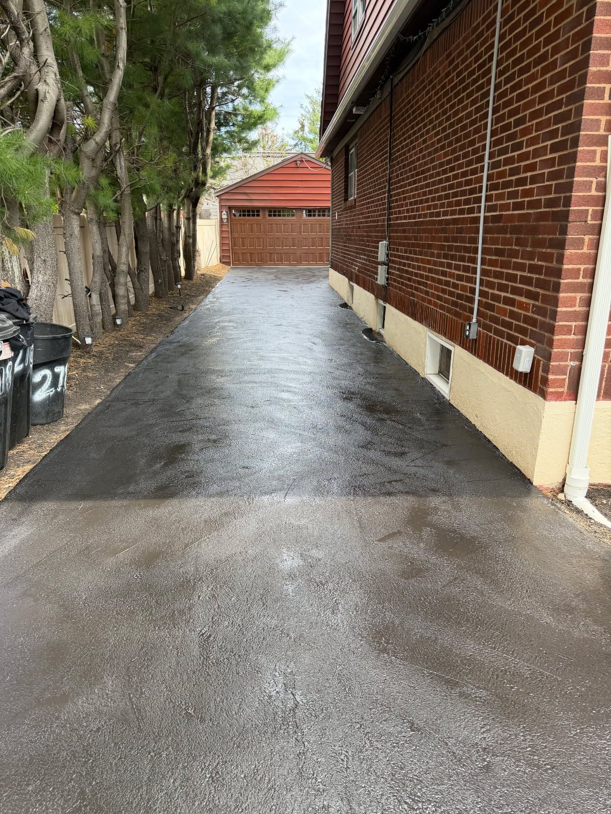 Narrow driveway beside a red brick wall and trees, leading to a small garage or shed at the end.