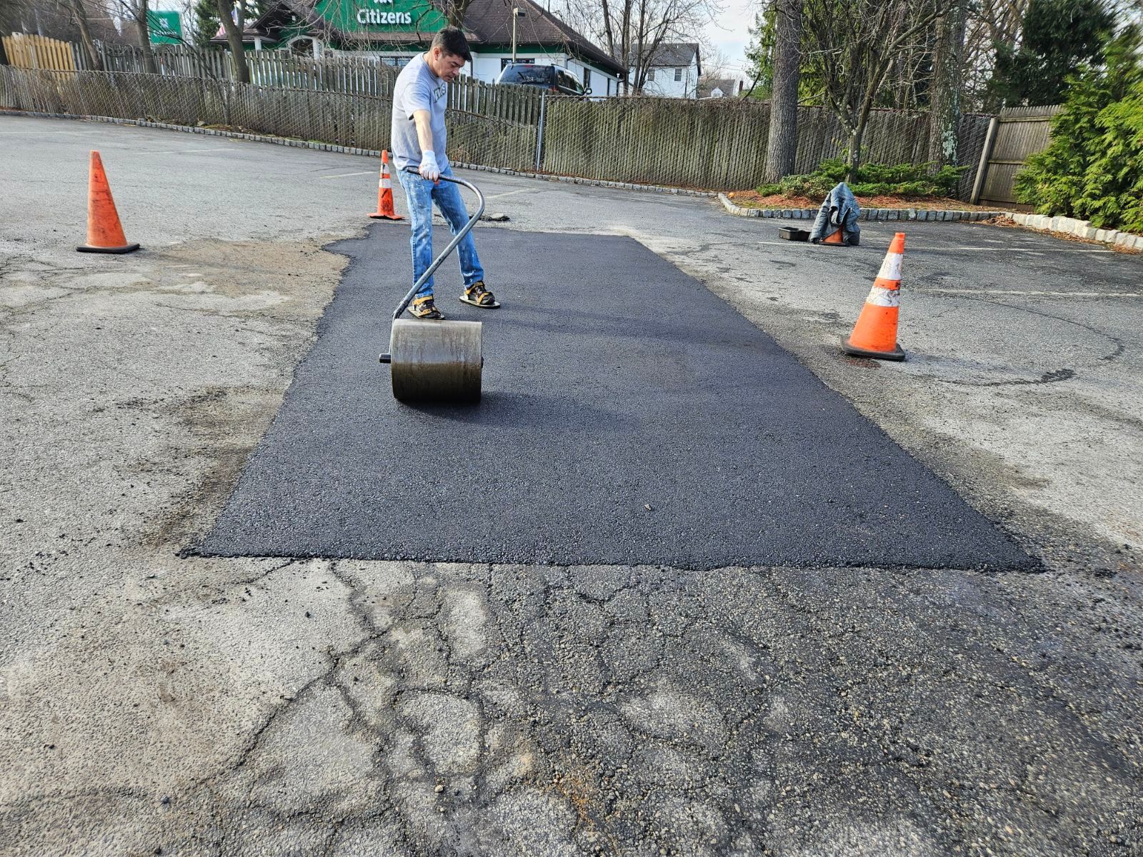 Worker rolling asphalt on a road repair site with traffic cones.