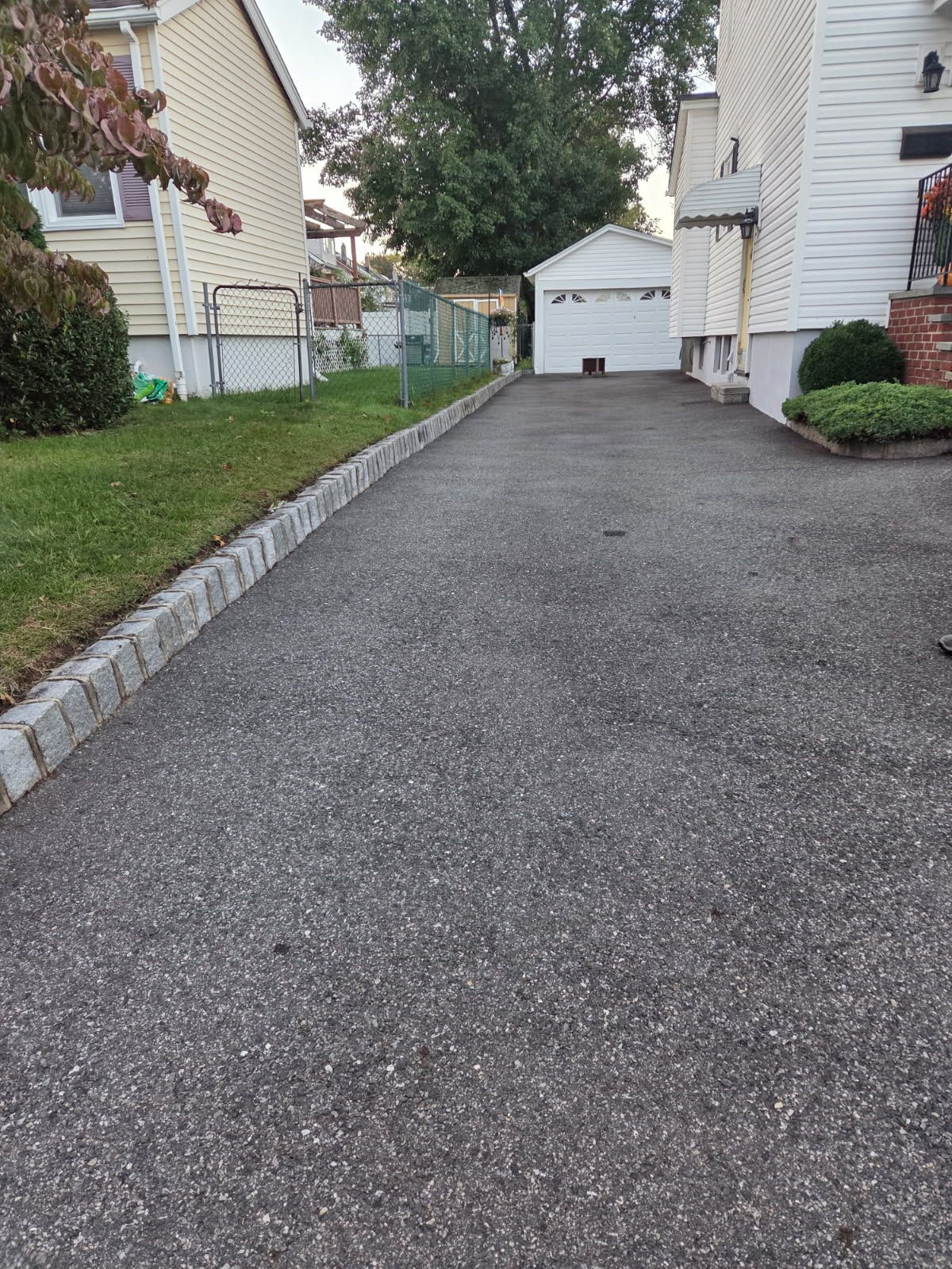 Narrow asphalt driveway between houses leading to a white garage at the end.