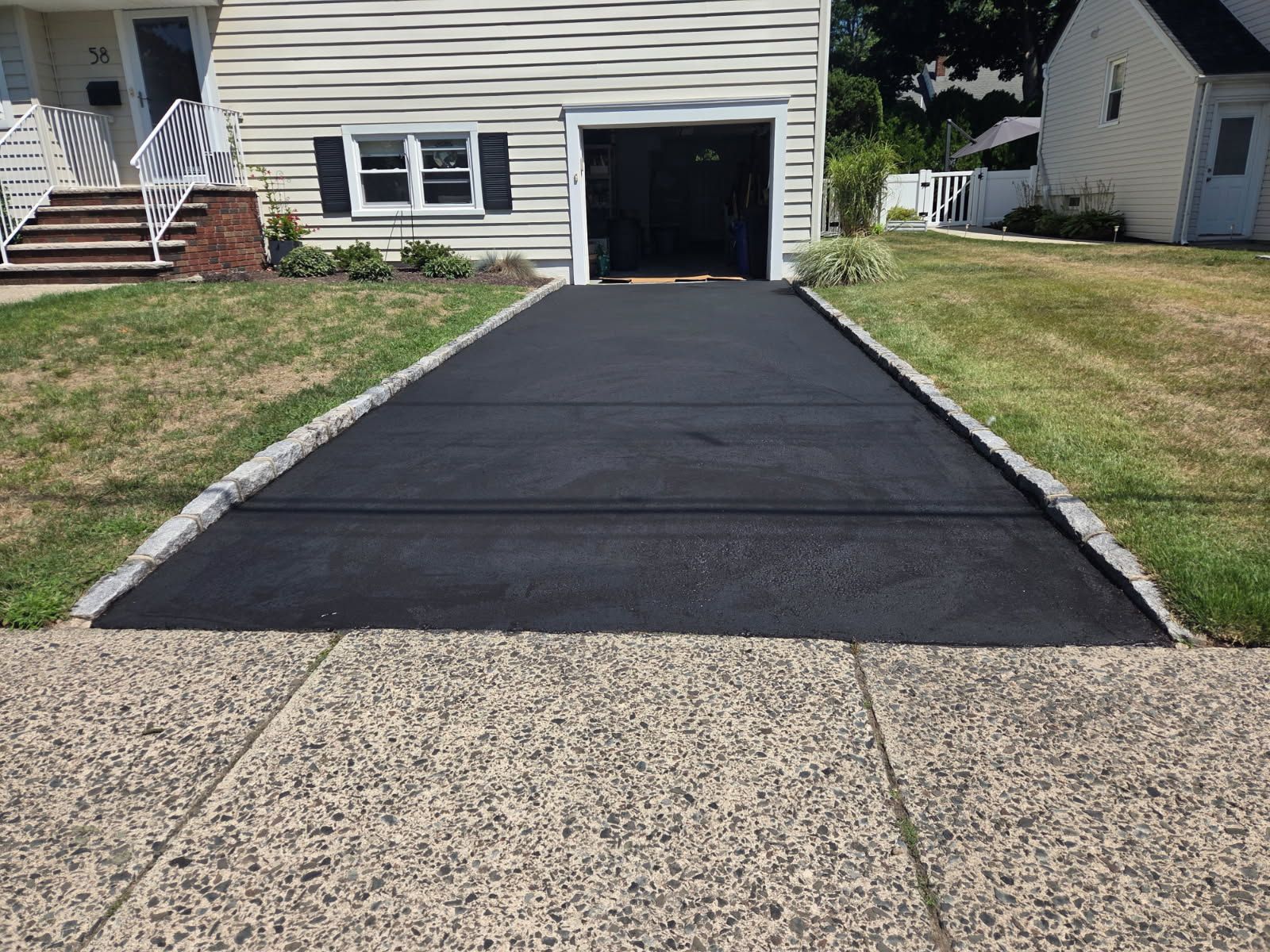 Freshly paved black driveway leading to an open garage beside a beige house