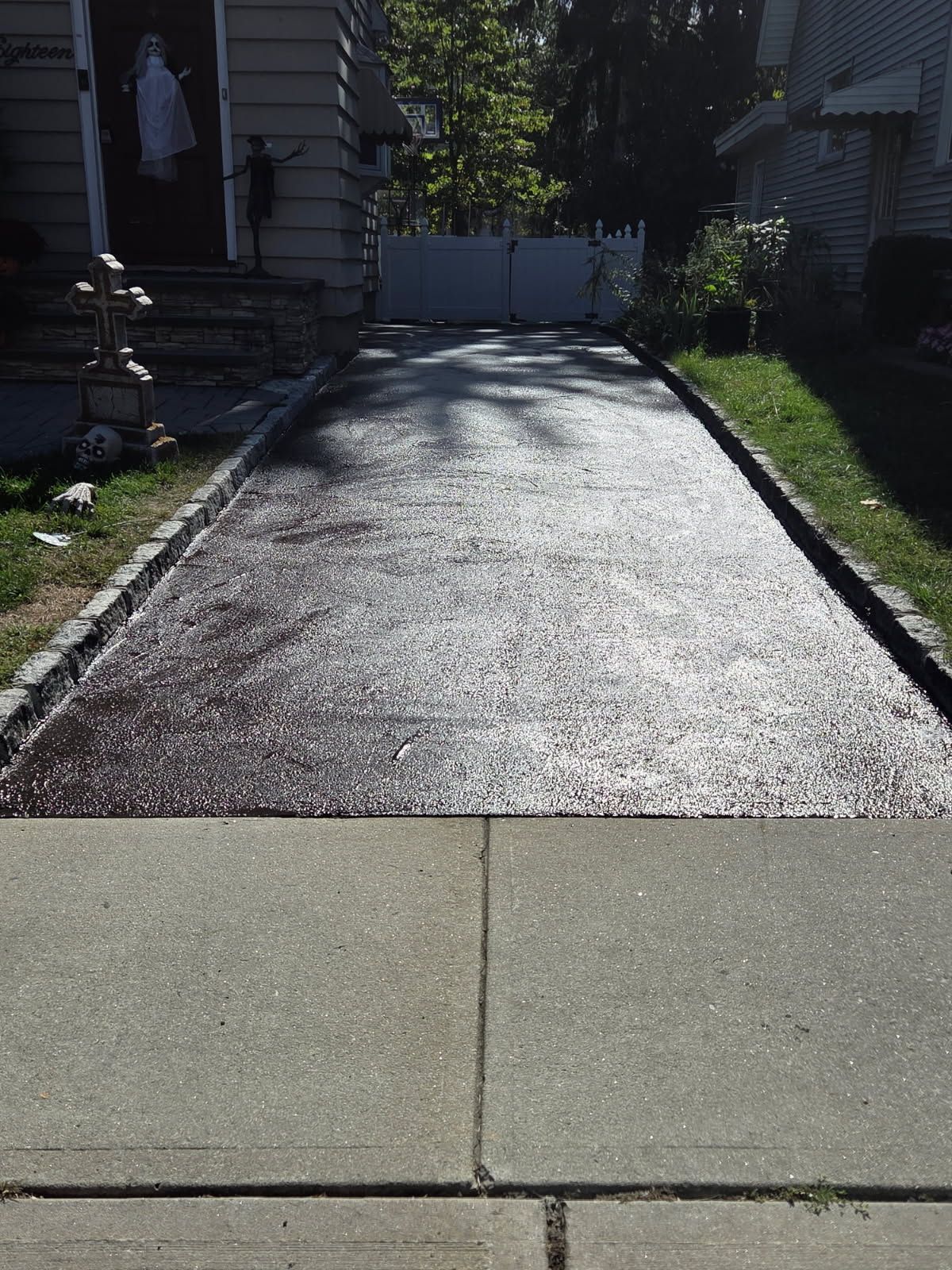Gravel driveway between houses, shaded by trees, leading to a gate at the end.