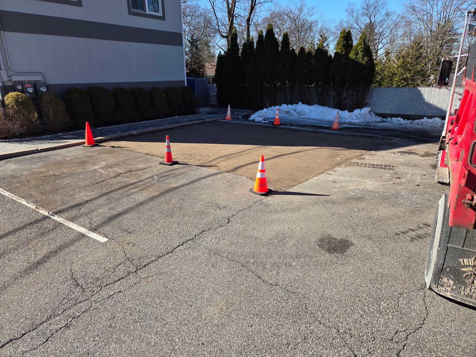 Orange traffic cones marking a closed asphalt parking area beside a building, with snow along the edge