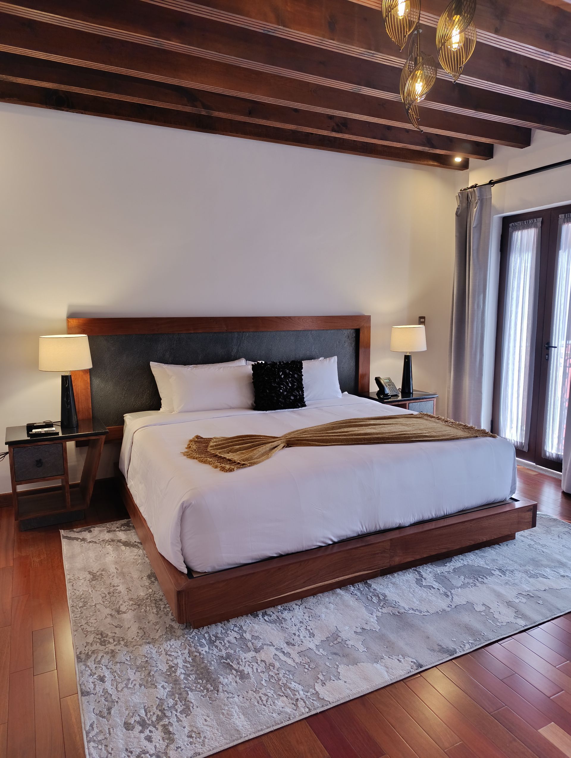 Dormitorio con cama grande, vigas de madera, dos lámparas de noche y alfombra.