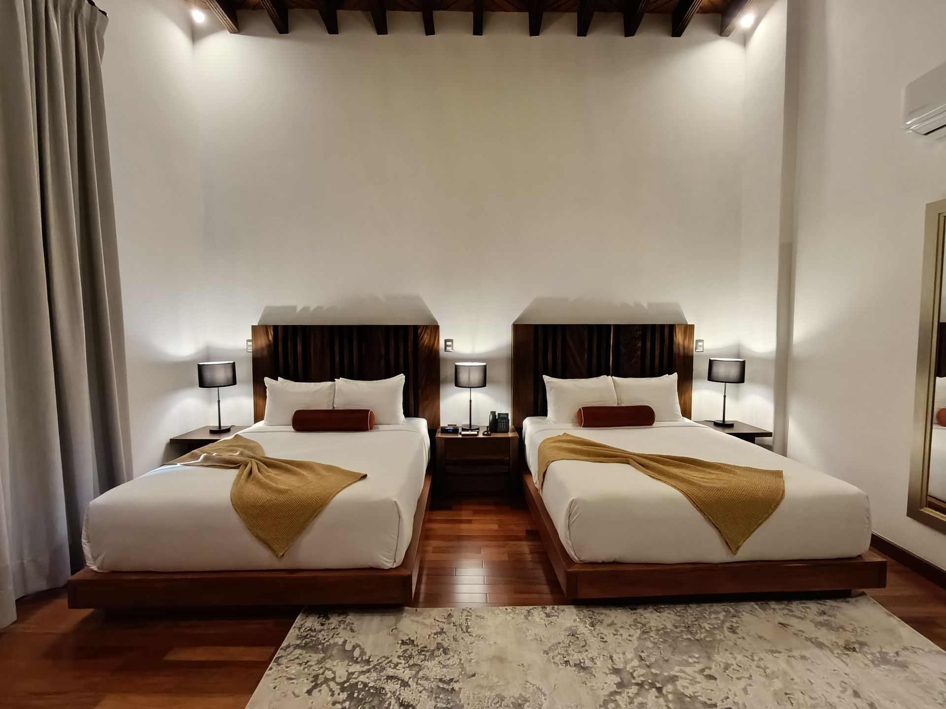Dos camas en una habitación de hotel con detalles de madera, lámparas y una alfombra.