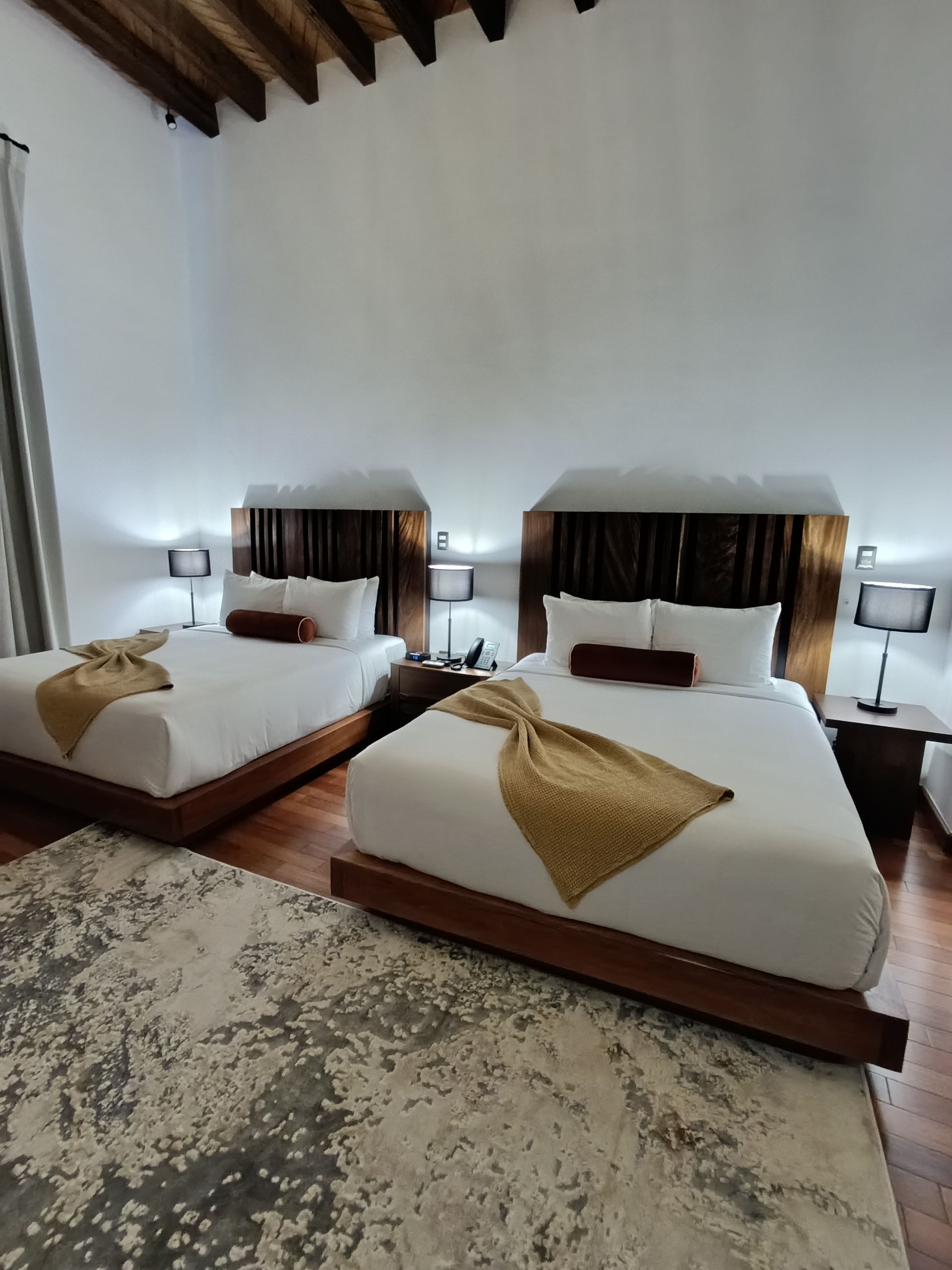Dos camas queen en una habitación de hotel con ropa de cama blanca y cabeceros y suelos de madera de color marrón.