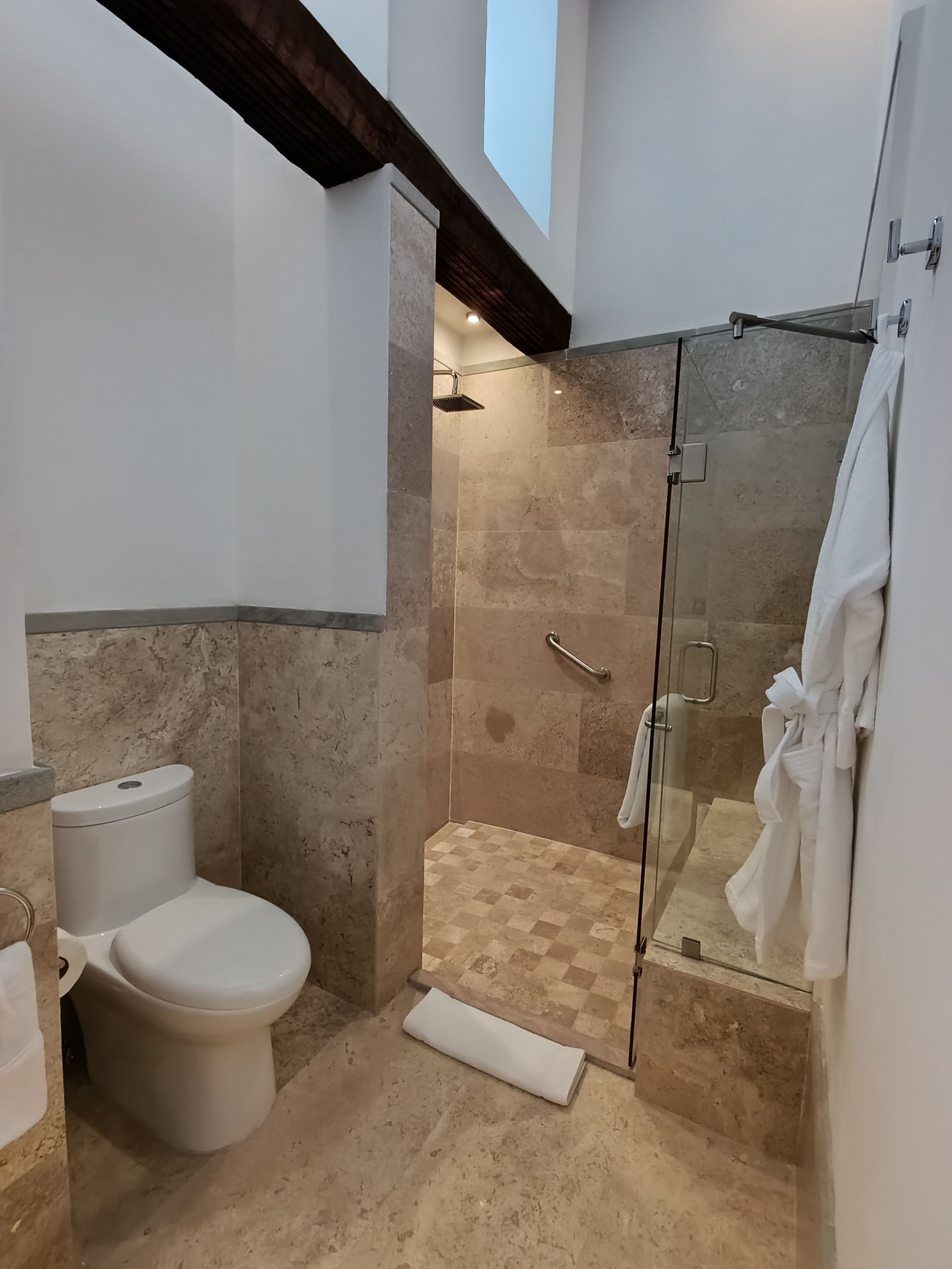 Baño con inodoro, ducha a ras de suelo, paredes de piedra y vigas de madera.