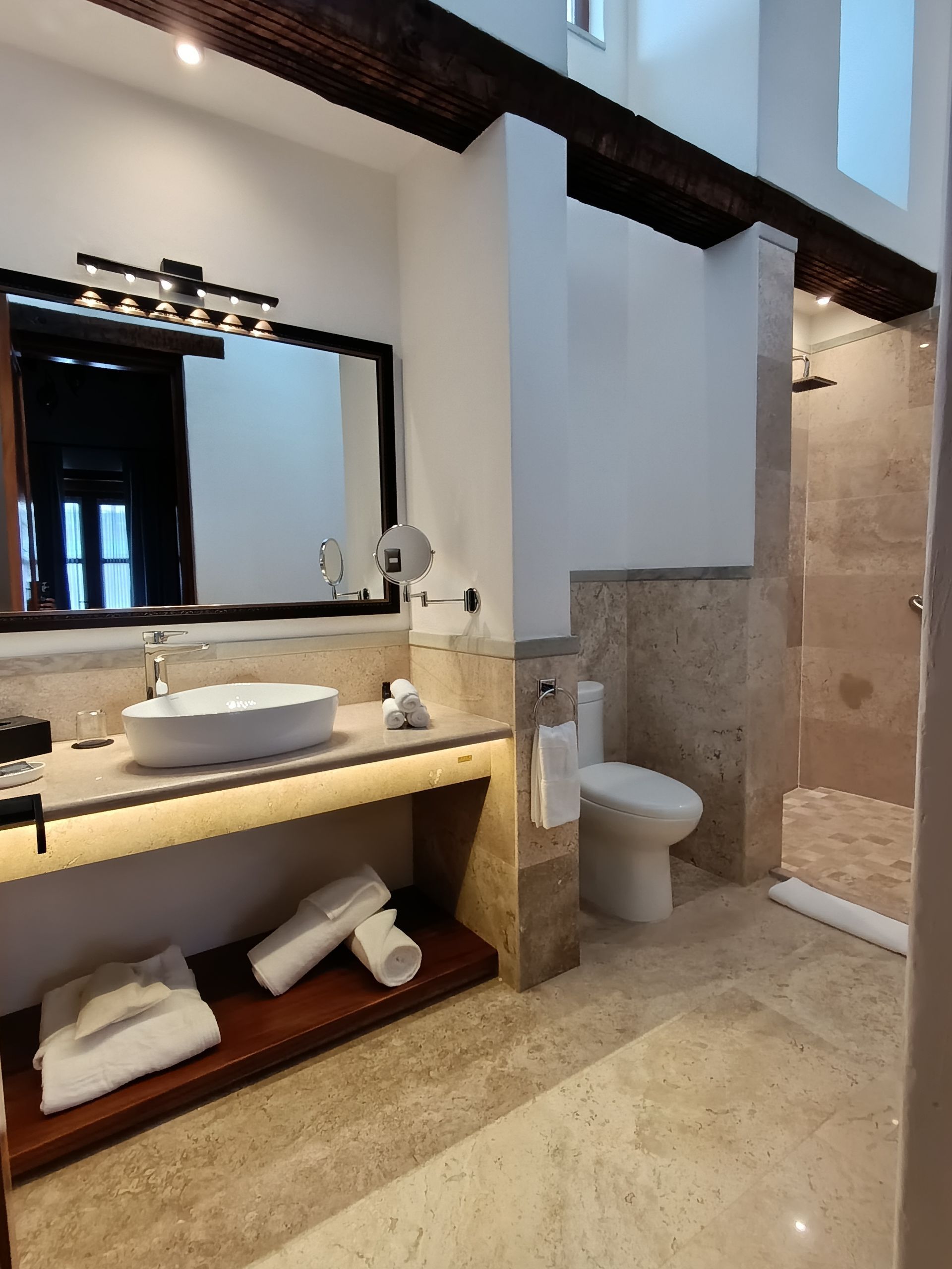 Baño con paredes de piedra, inodoro, ducha y lavabo con espejo.