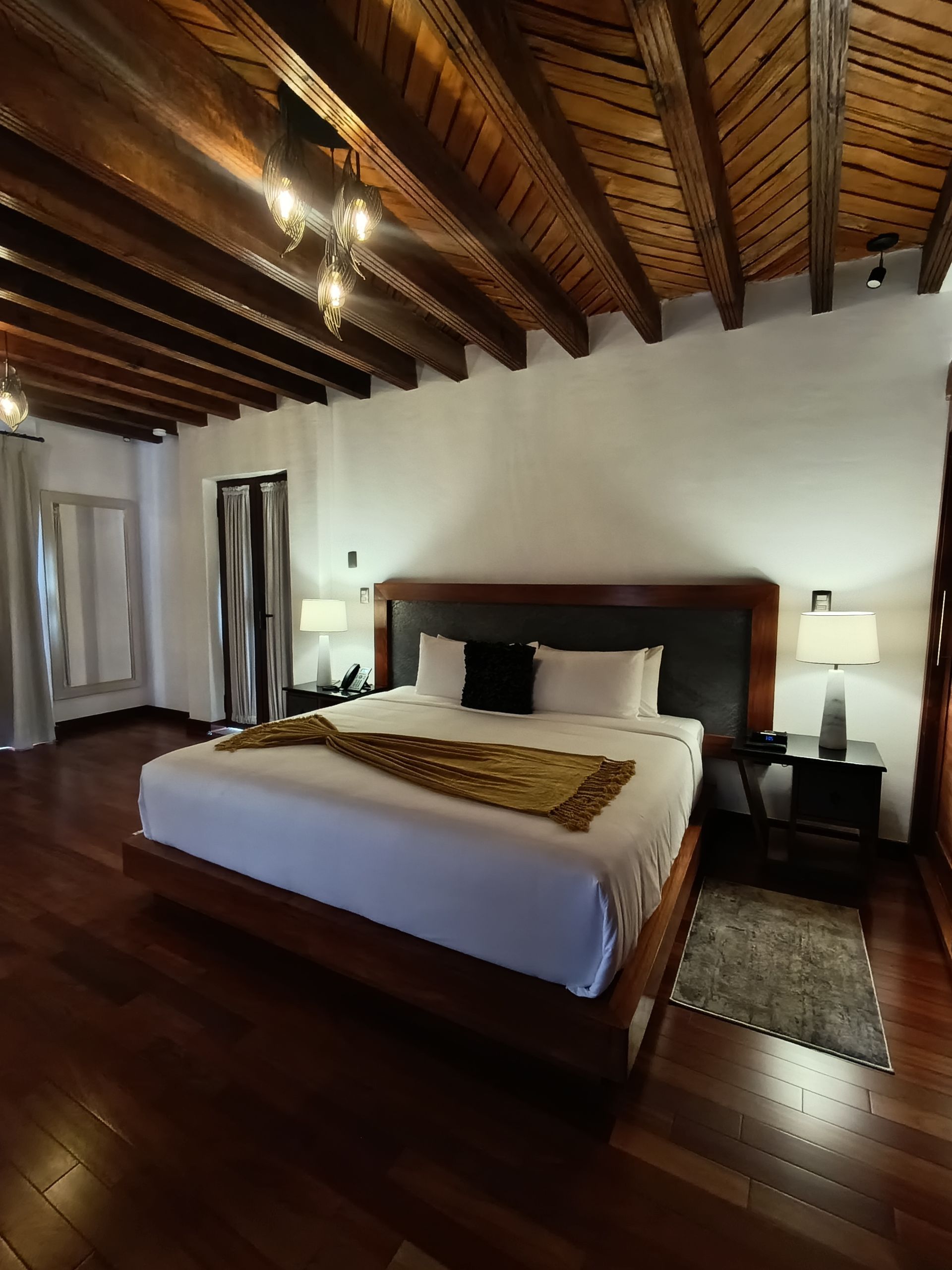 Dormitorio con cama grande, suelo y techo de madera. Dos lámparas flanquean el cabecero.