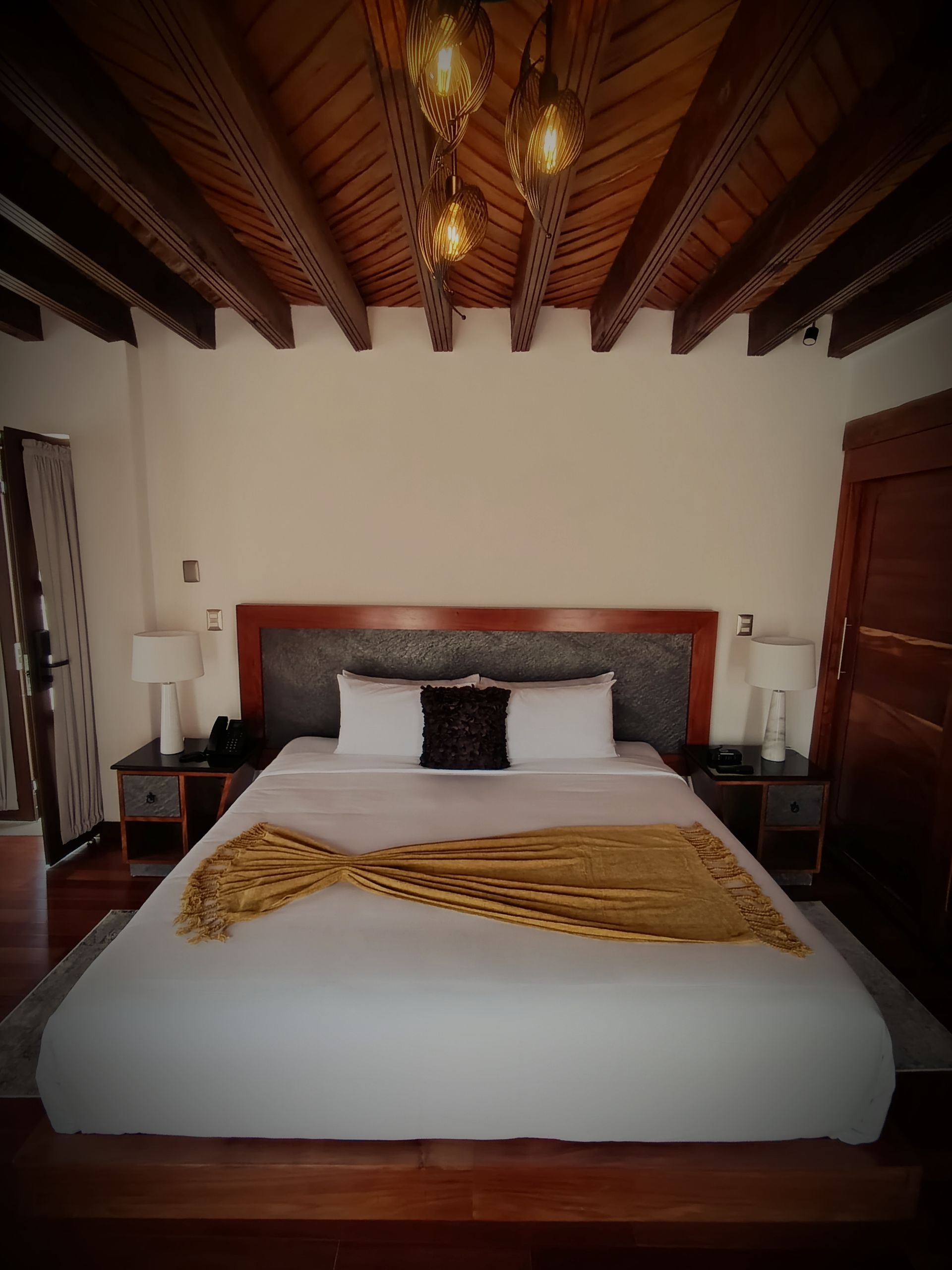 Dormitorio con cama grande, mesitas de noche y techo de madera con lámparas colgantes.
