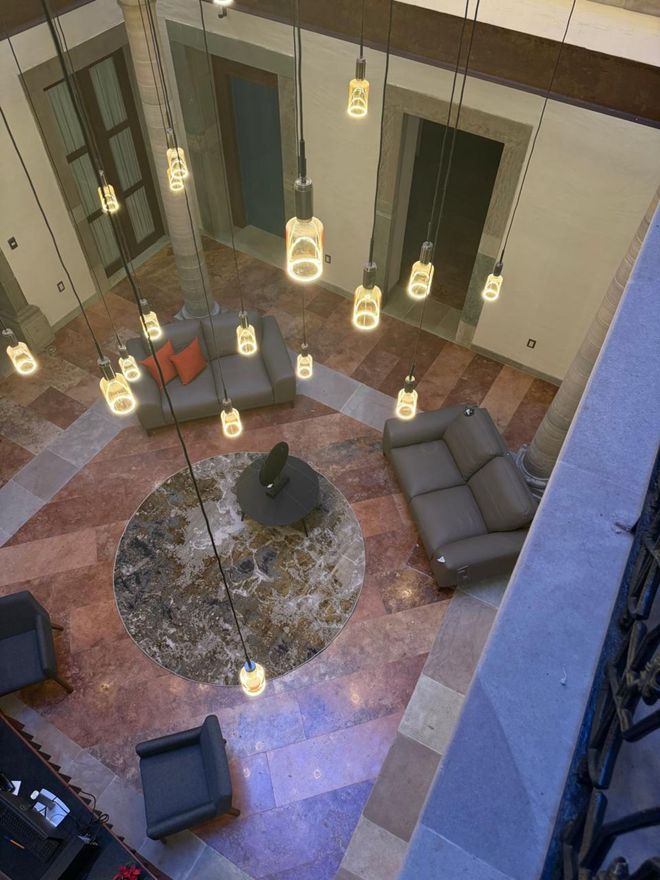 Vista aérea del lobby de un hotel con sofás, sillas, piso de mármol y luces colgantes.