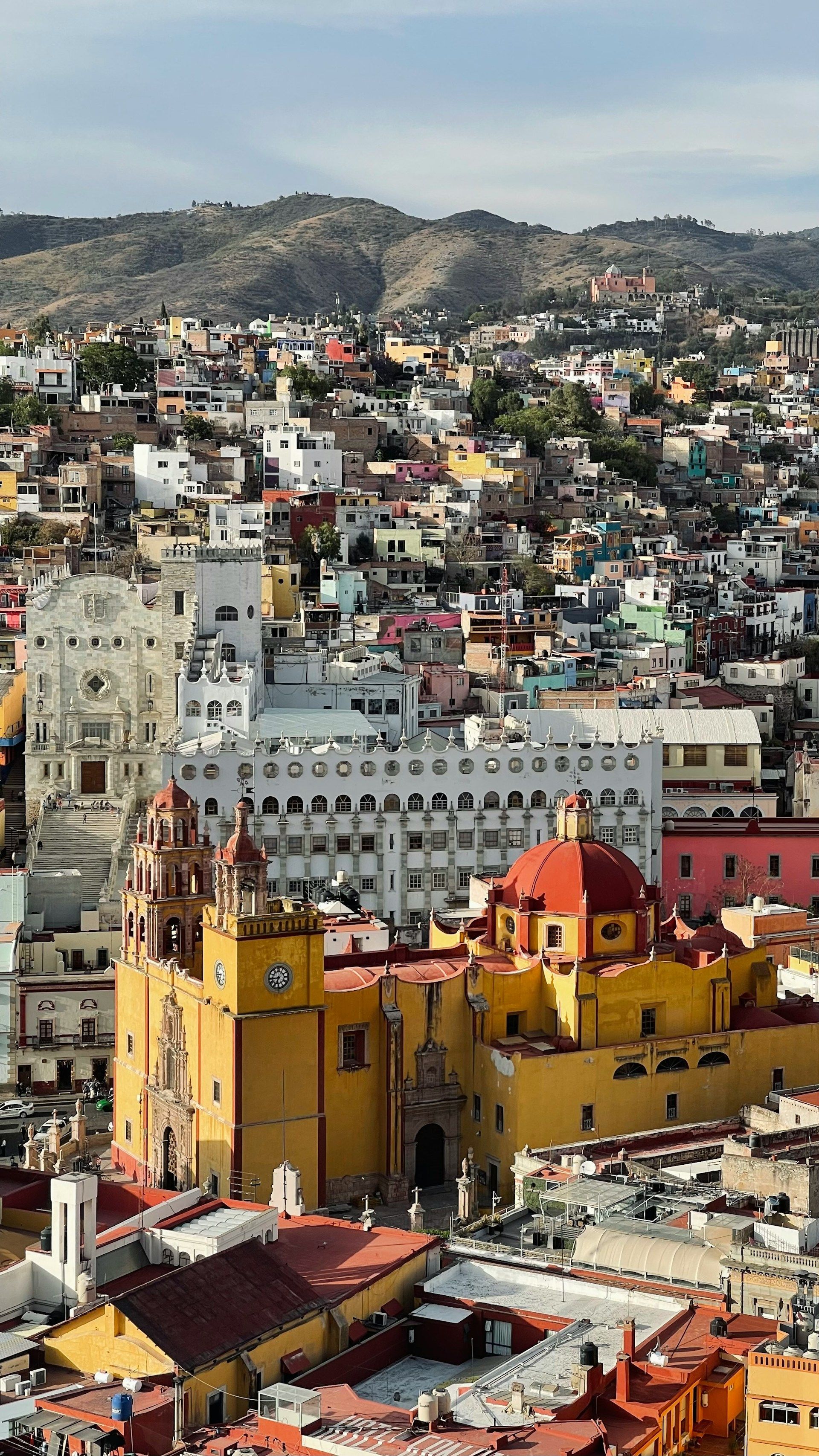 Paisaje urbano vibrante con una iglesia amarilla y una cúpula roja, edificios muy juntos en una ladera bajo un cielo brumoso.