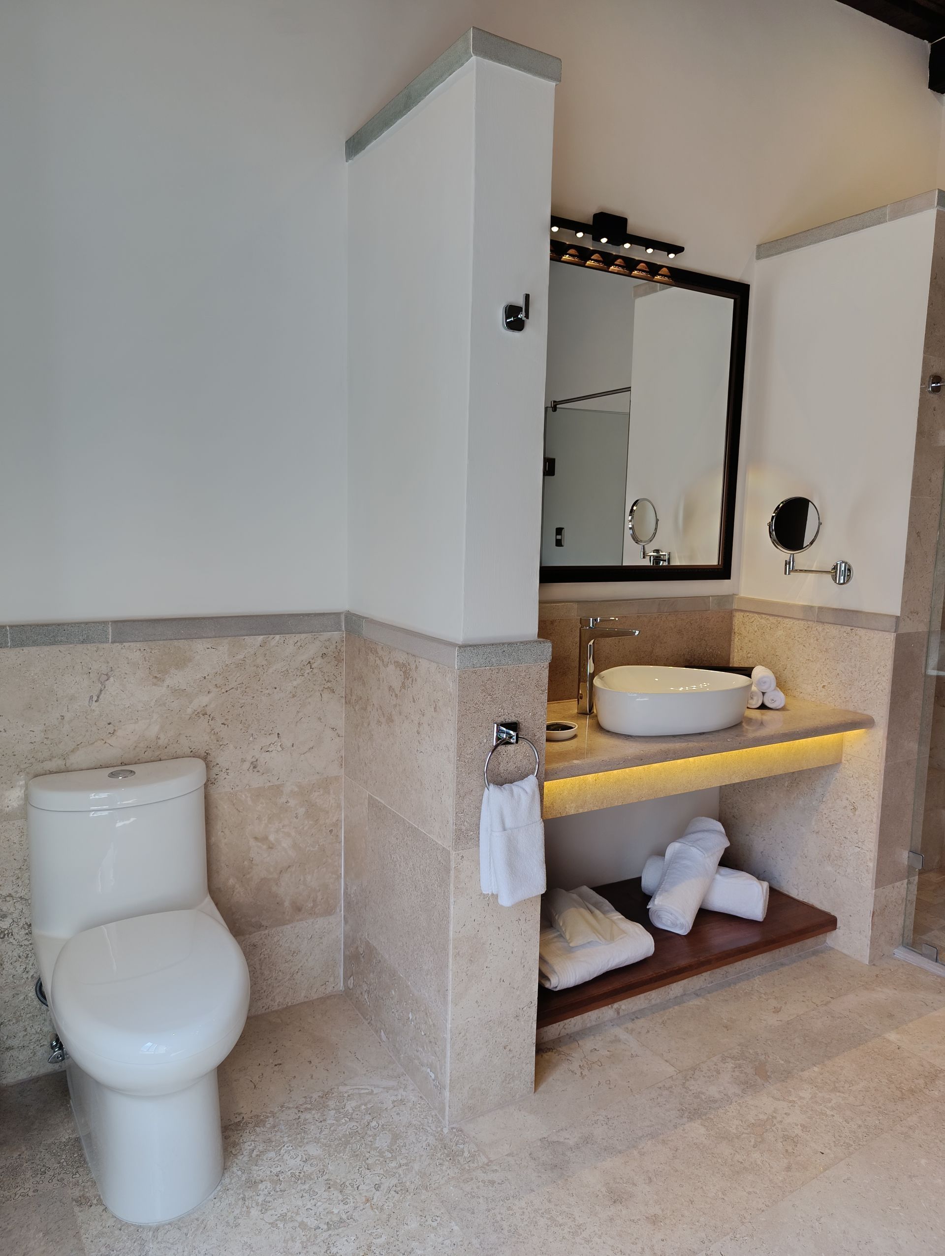 Baño con inodoro blanco, lavabo, espejo y paredes y suelo de azulejos de color beige.