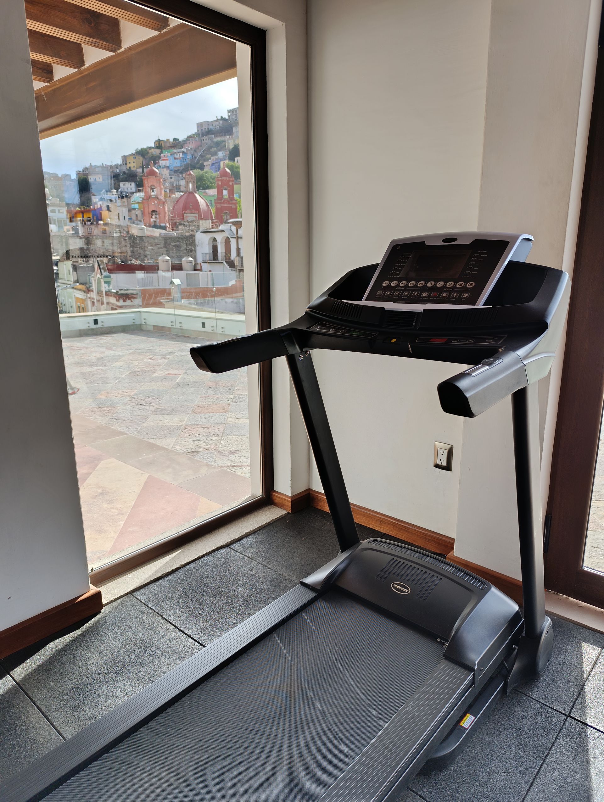 Cinta de correr junto a una ventana con vistas a un paisaje urbano. Máquina negra con pantalla oscura.