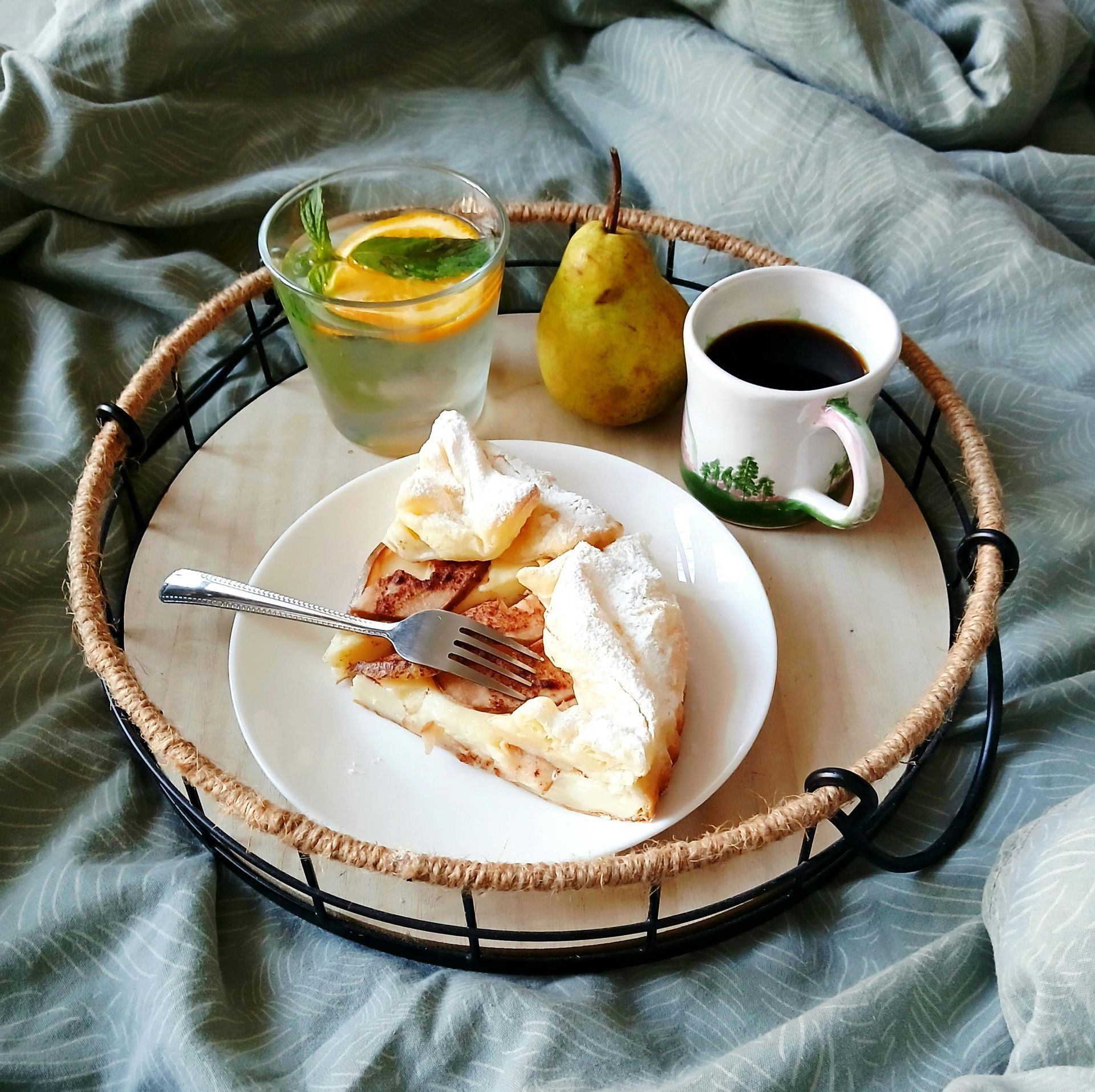 Bandeja de desayuno en la cama: rebanada de tarta, café, agua con limón, pera.