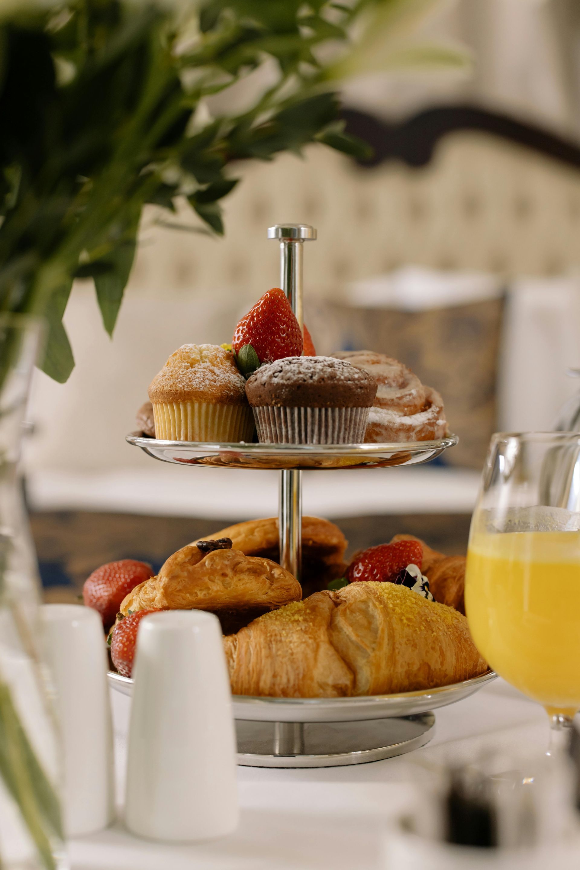Bandeja de dos niveles con muffins, croissants y fresas, junto con jugo de naranja.