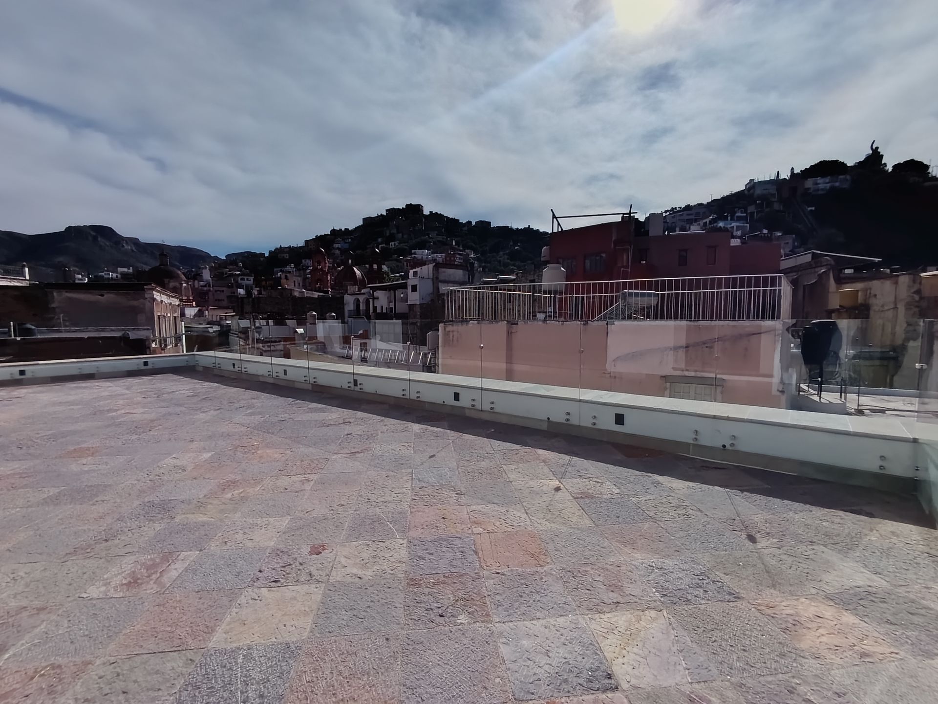 Vista desde la azotea de una ciudad con fondo de montañas en un día nublado.