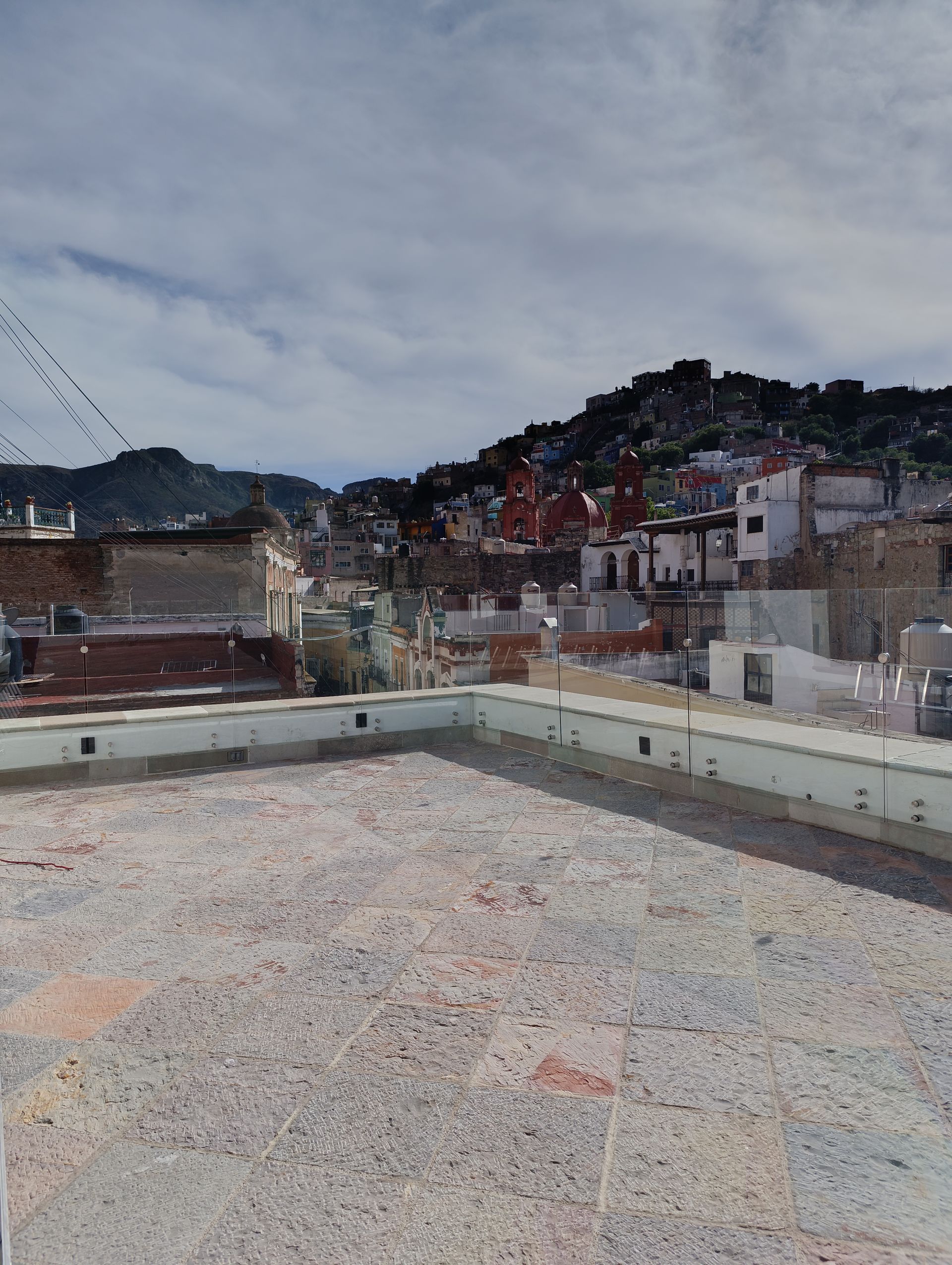 Vista desde los tejados de un pueblo en la ladera bajo un cielo nublado. Los edificios se agrupan en la ladera.