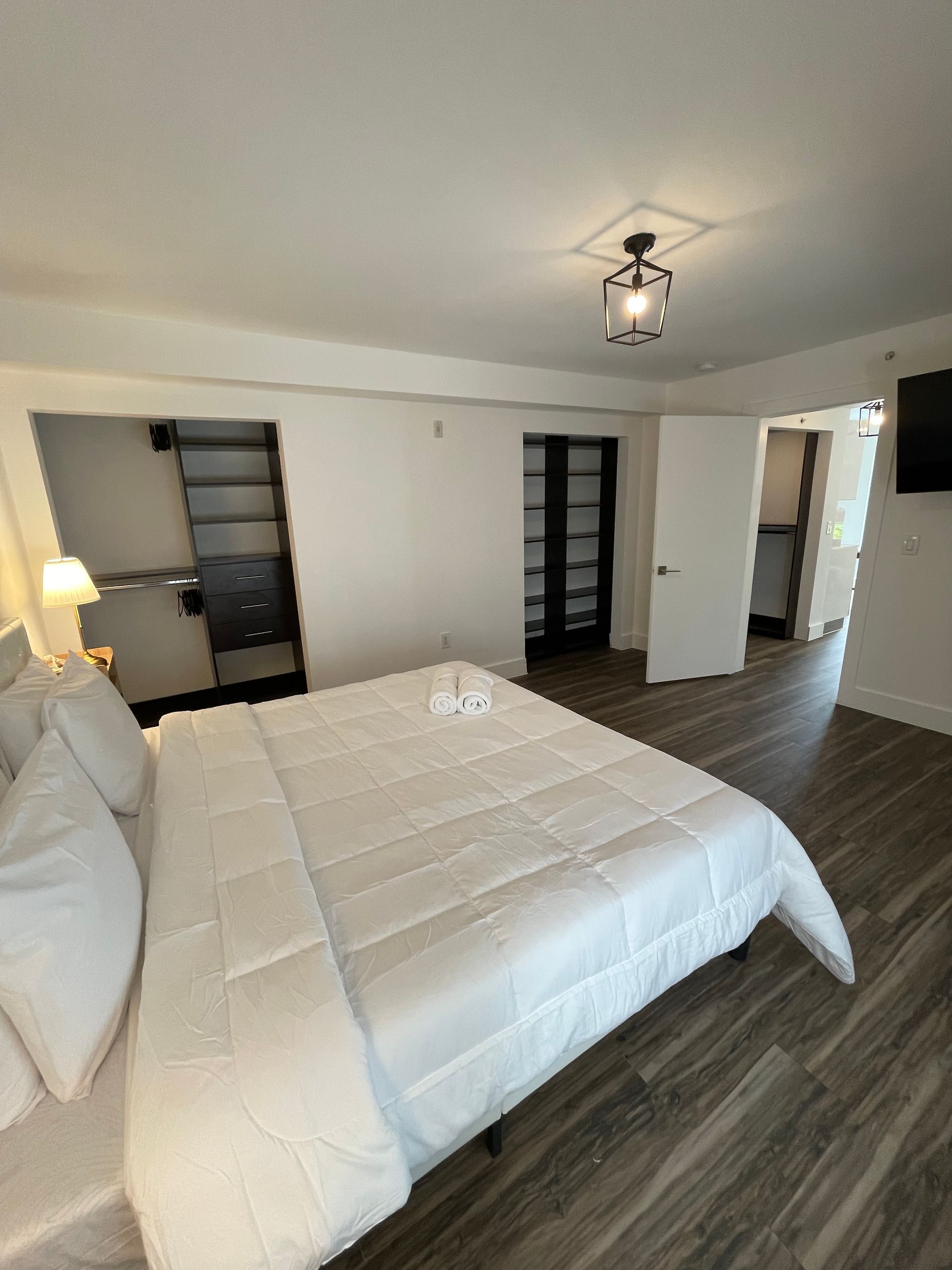 Bedroom with a white bed, wooden floor, and a dark closet.