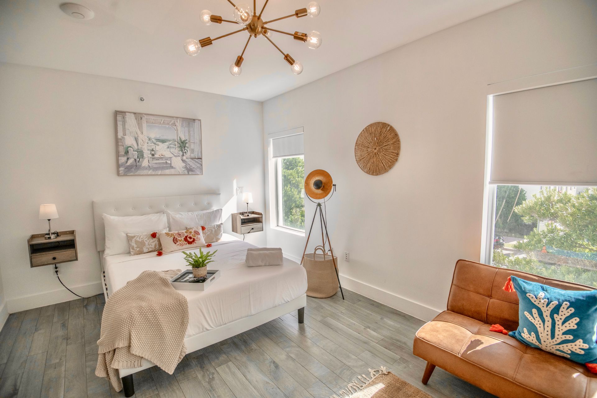 Bedroom with white walls, bed, brown sofa, wicker decor, and a light fixture.