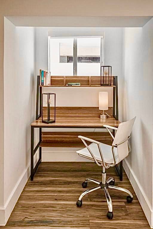A home office nook with a desk, chair, and shelving. White walls, wood desk, and window.