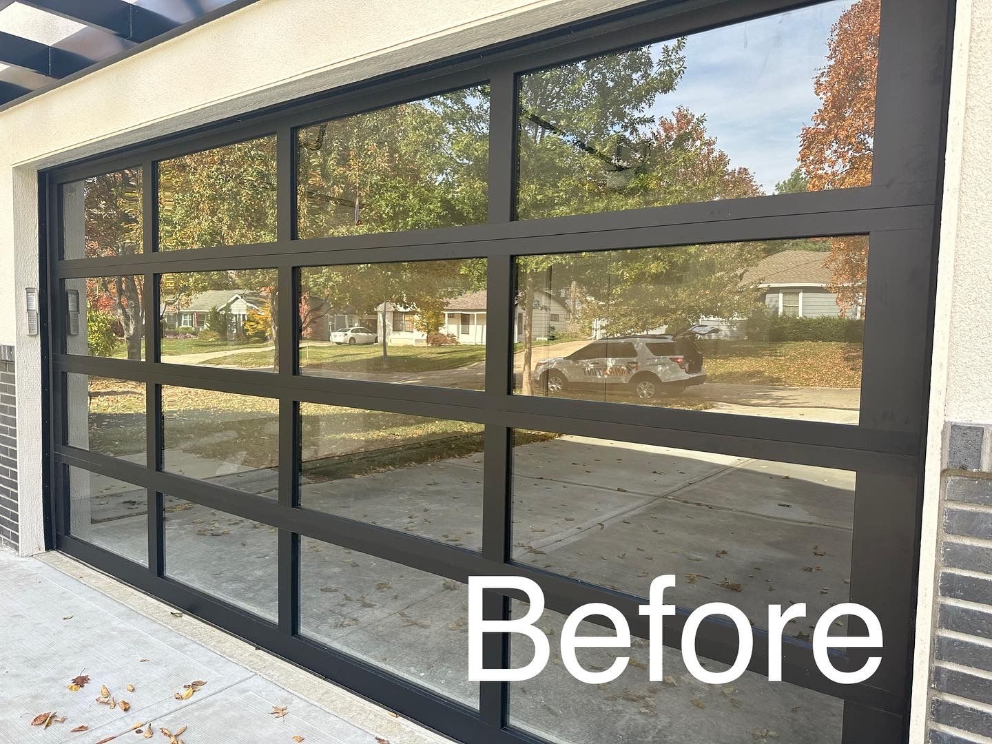 Black-framed glass garage door reflecting the outdoors, labeled 