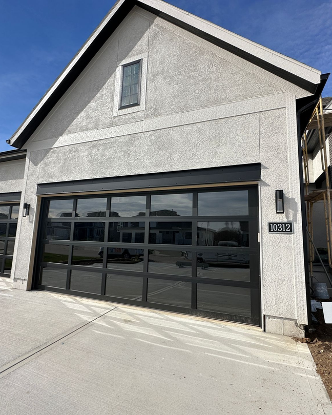 Modern house exterior with a black-framed glass garage door, light stucco, and a small window.