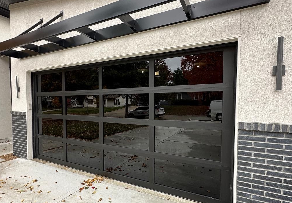 Black-framed glass garage door reflecting the street. Modern facade with brick accents and awning.