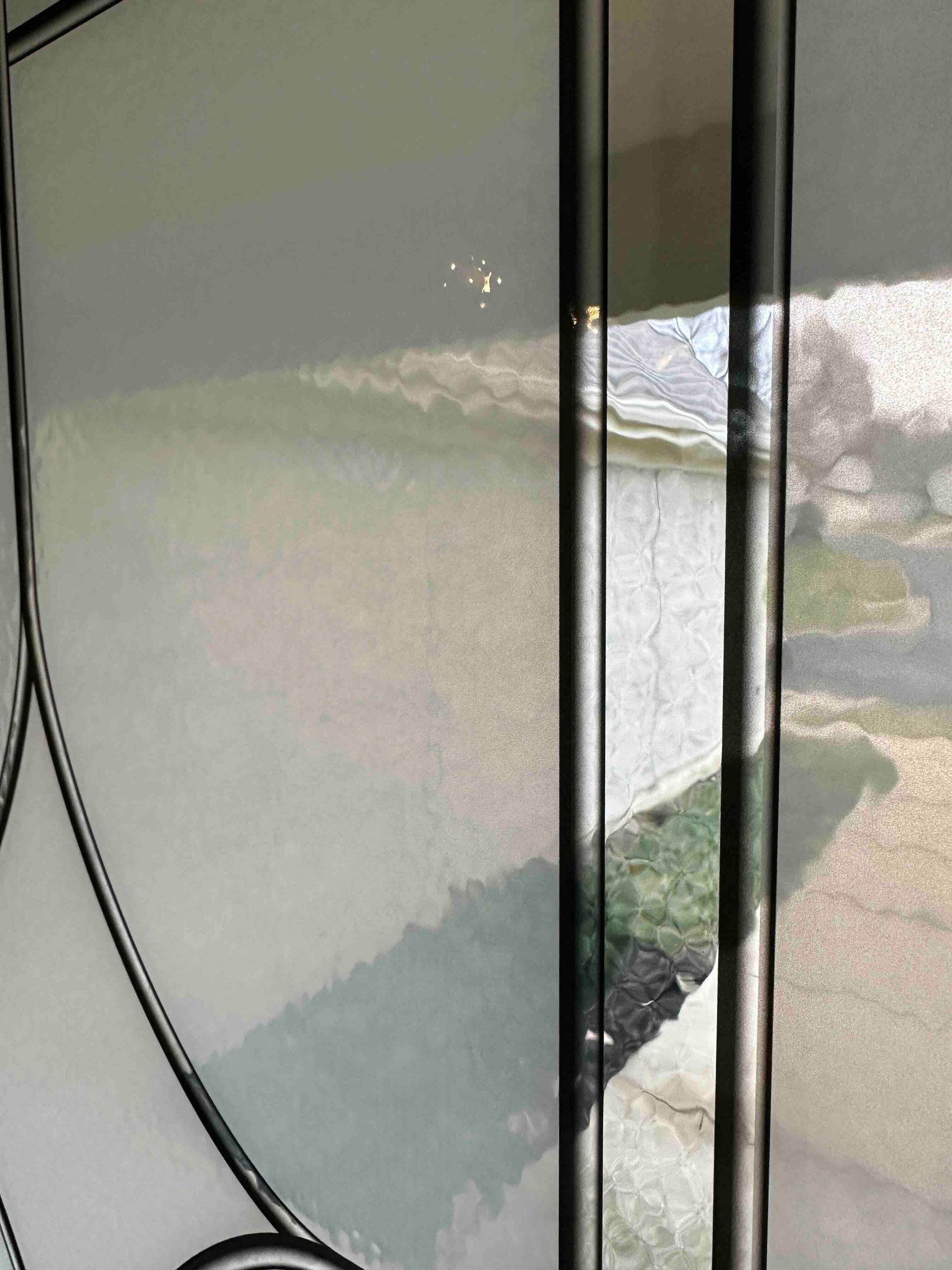 Blue diamond-patterned stained-glass window in a white door, reflecting a house and landscape.