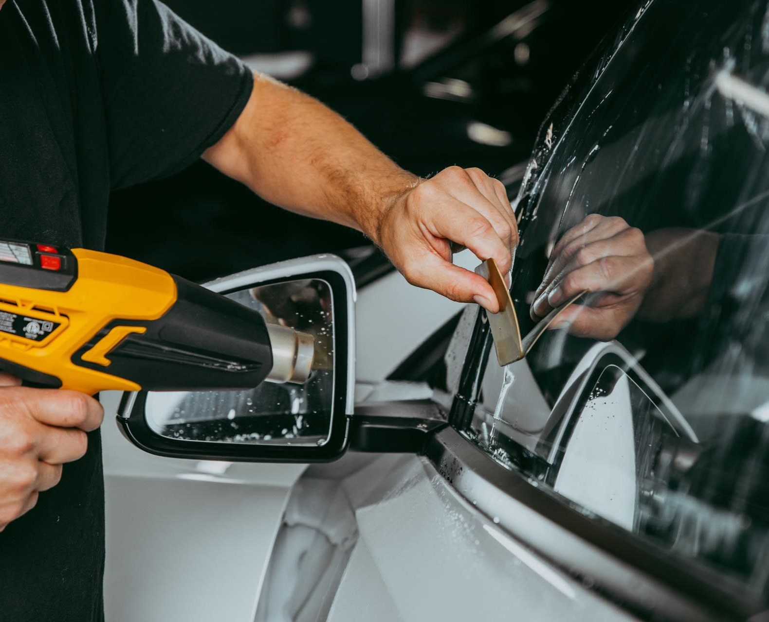 A person is applying tint to the windshield of a gray Ford SUV in a garage.