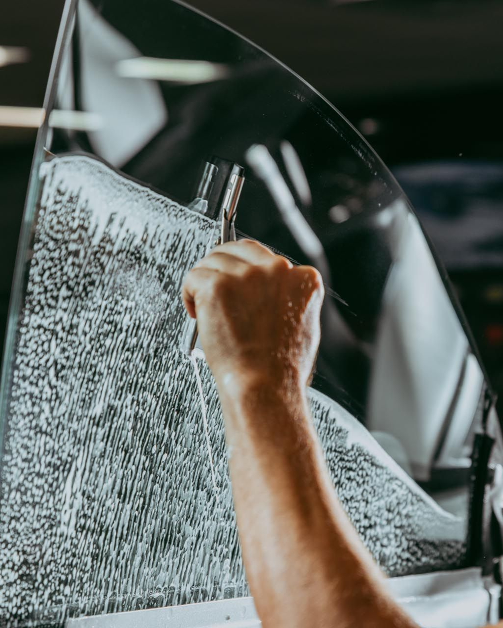 Hand applying tint film to a car window. Film is wet, tool held to smooth it.