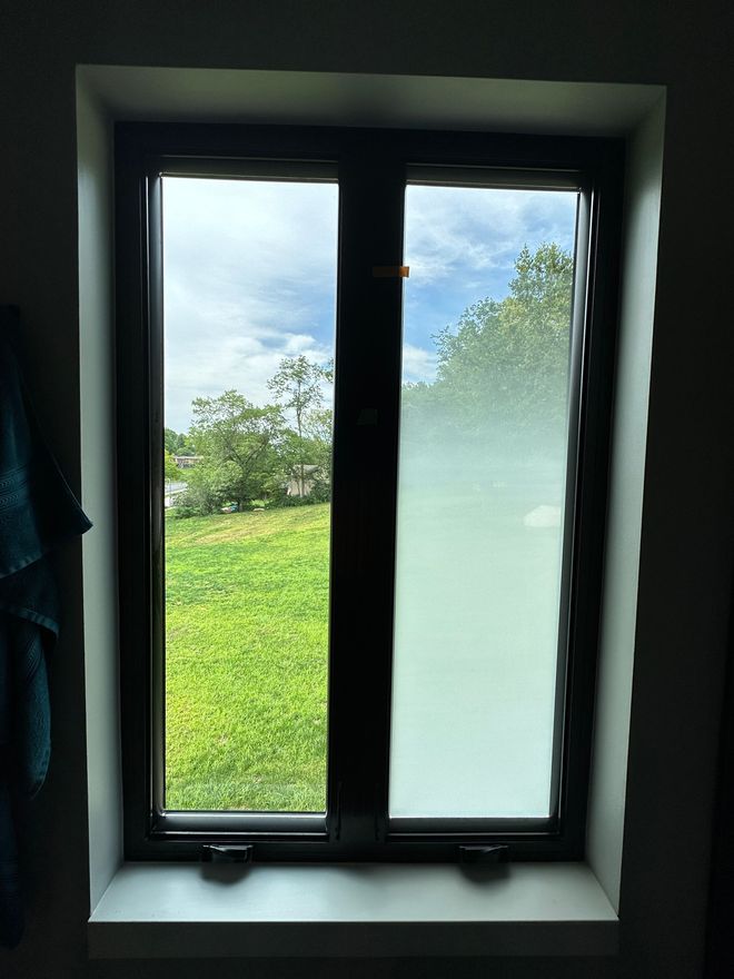 Window with clear and frosted panes, showing a yard with grass and sky.