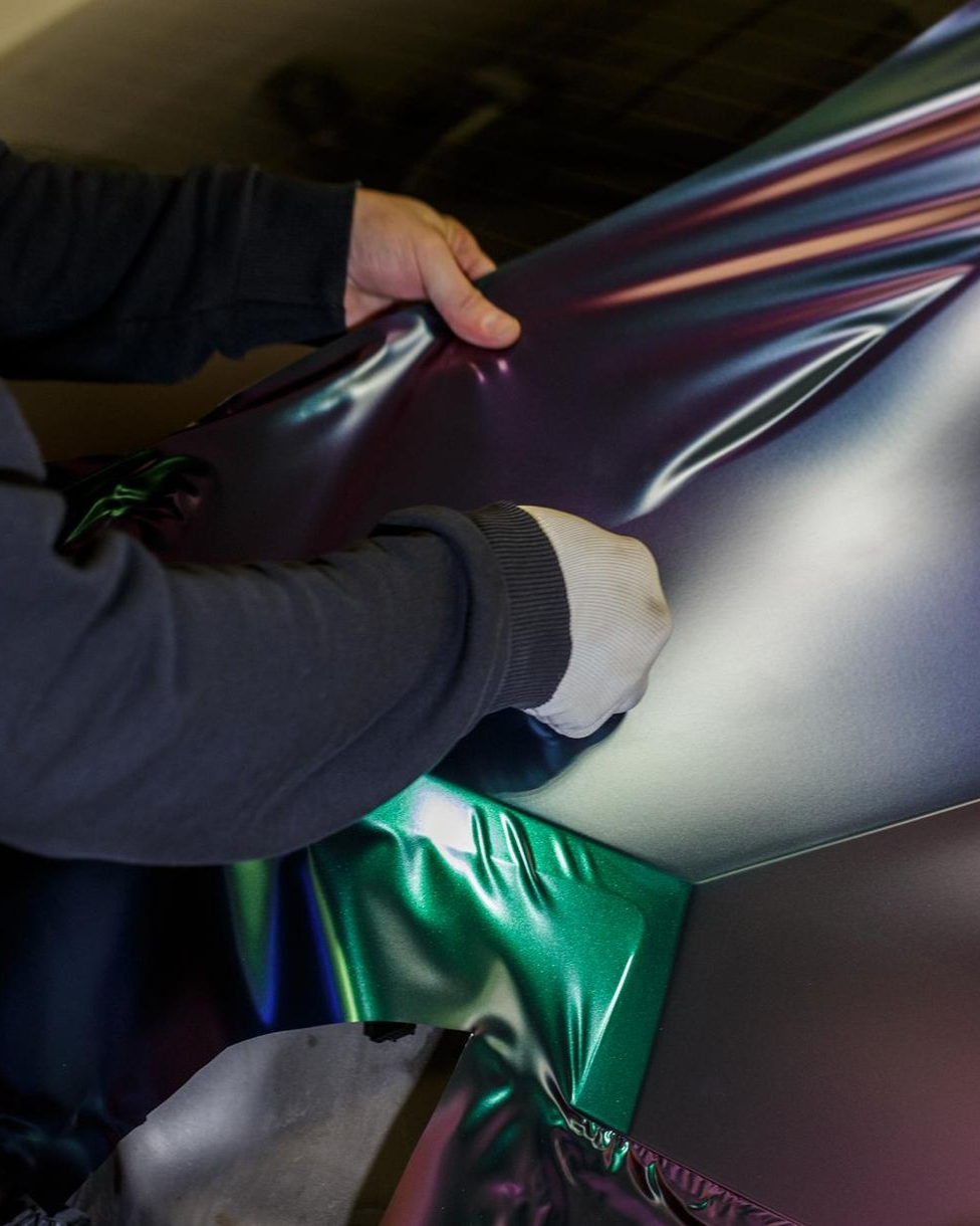 Person in black sleeves and a white glove stretches iridescent film over a surface.